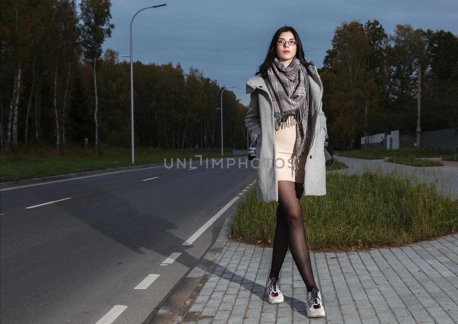 young girl in a gray coat stands near the road trying to stop a car by raddnatt