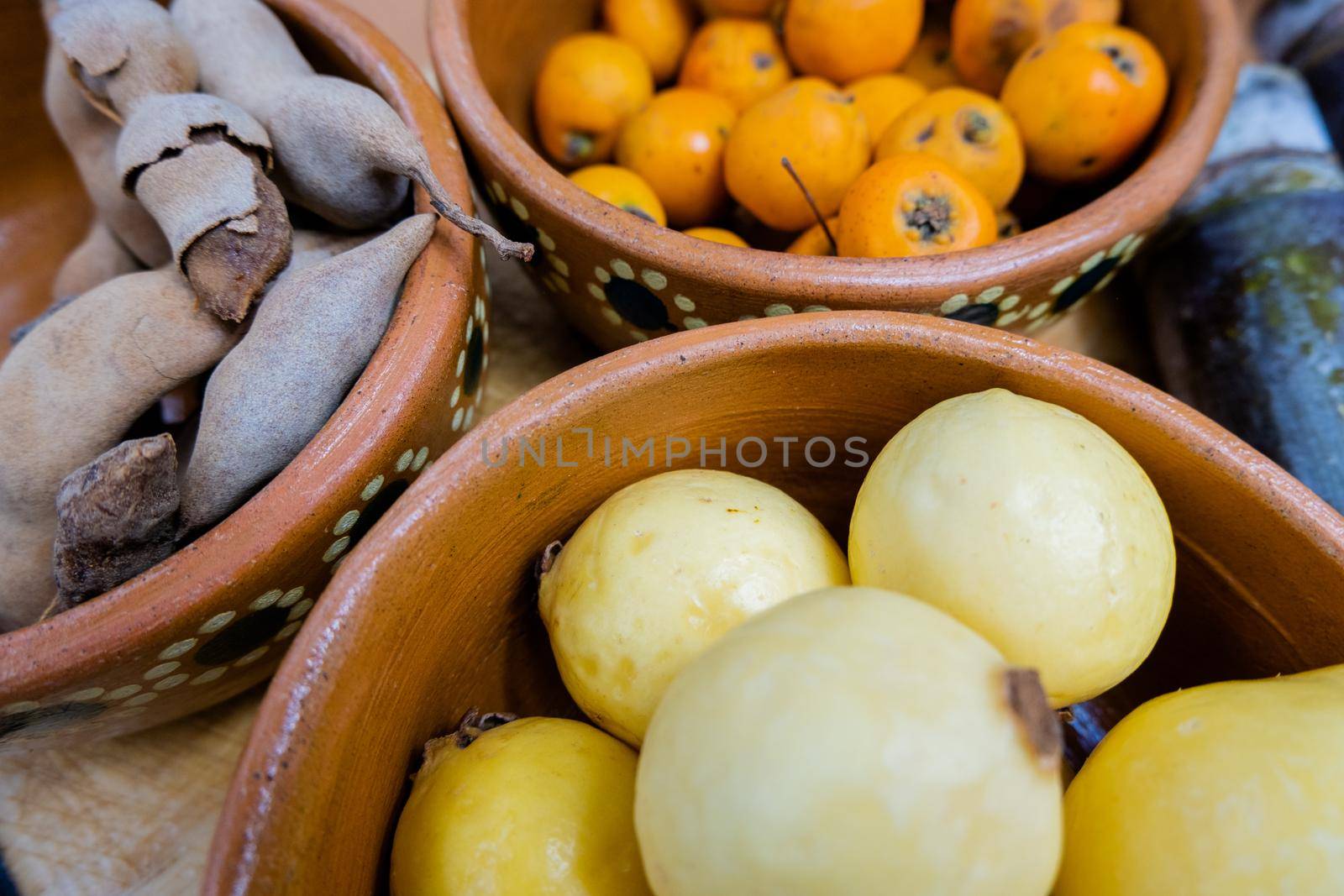 Fresh yellow guavas, Mexican hawthorns, and tamarind in handmade clay bowls. Close-up of brown bowls of Mexican fruit. Traditional snack preparation