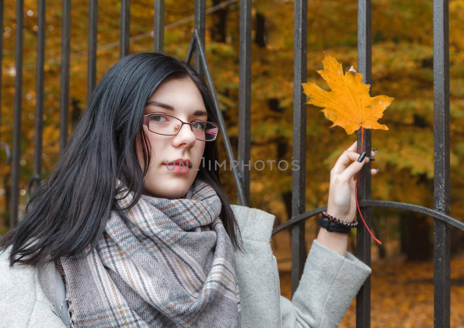 young girl holding a yellow maple leaf in her hand in the park in autumn. portrait closeup