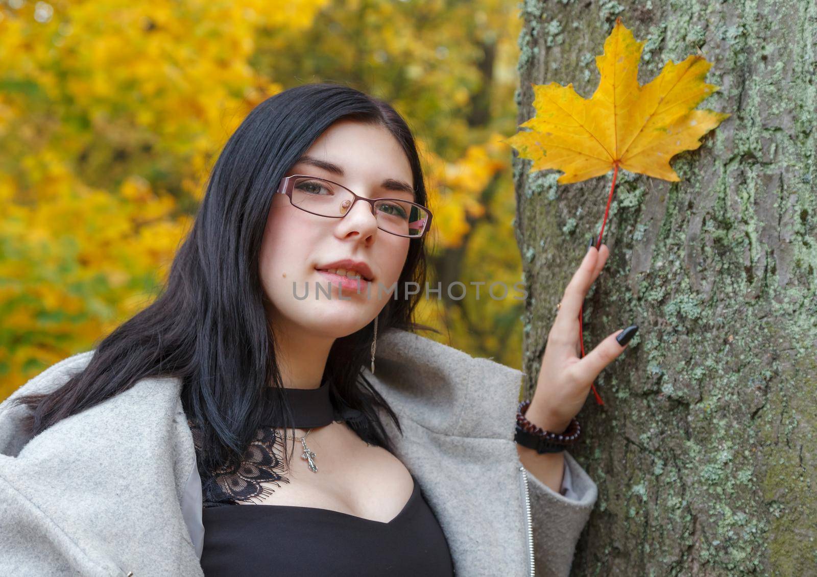 young girl holding a yellow maple leaf in her hand in the park in autumn. portrait closeup