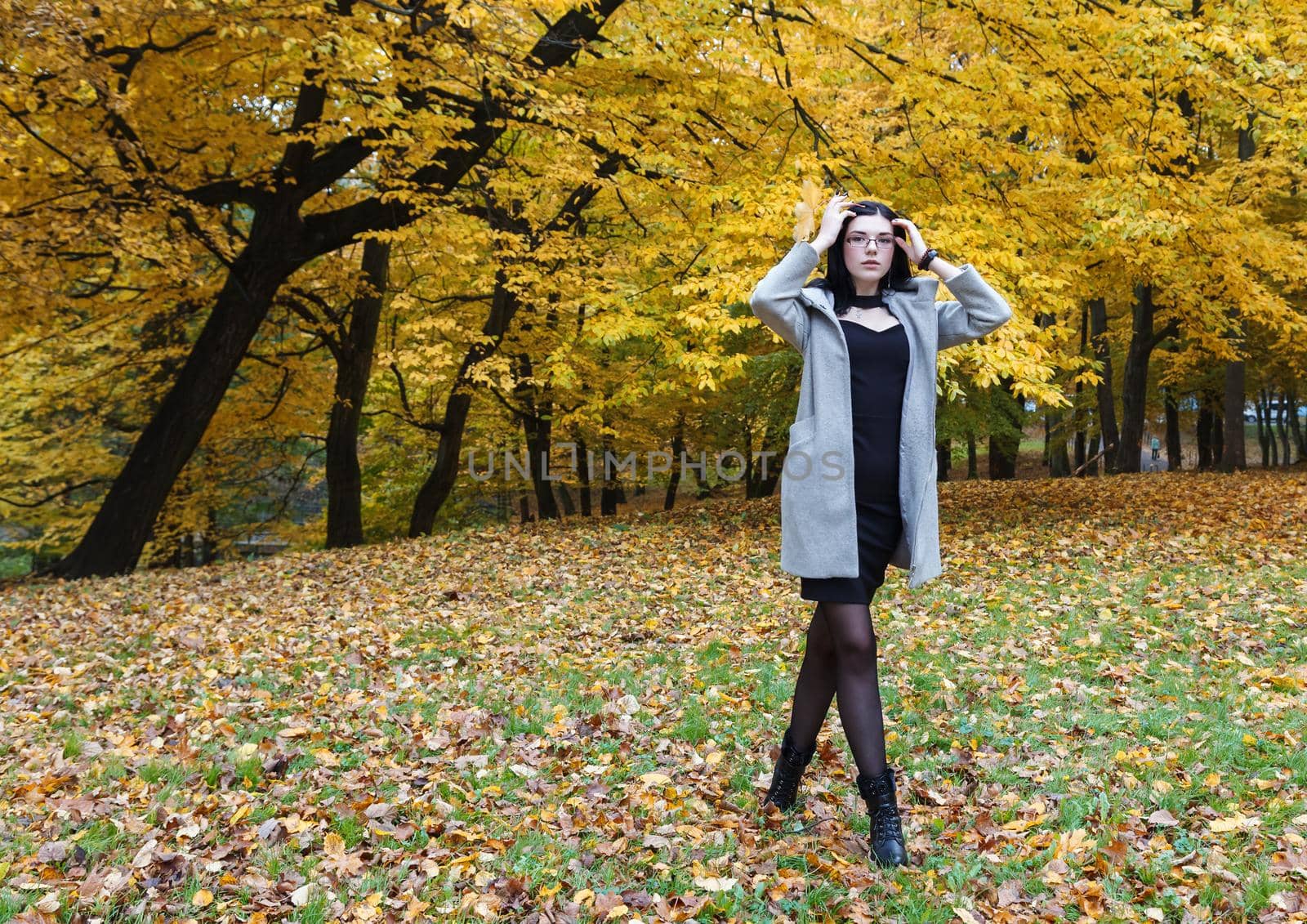 young girl in a gray coat standing on an alley in a city park on autumn day