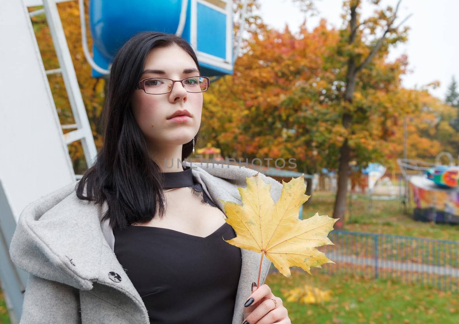 young girl holding a yellow maple leaf in her hand in the park in autumn. portrait closeup