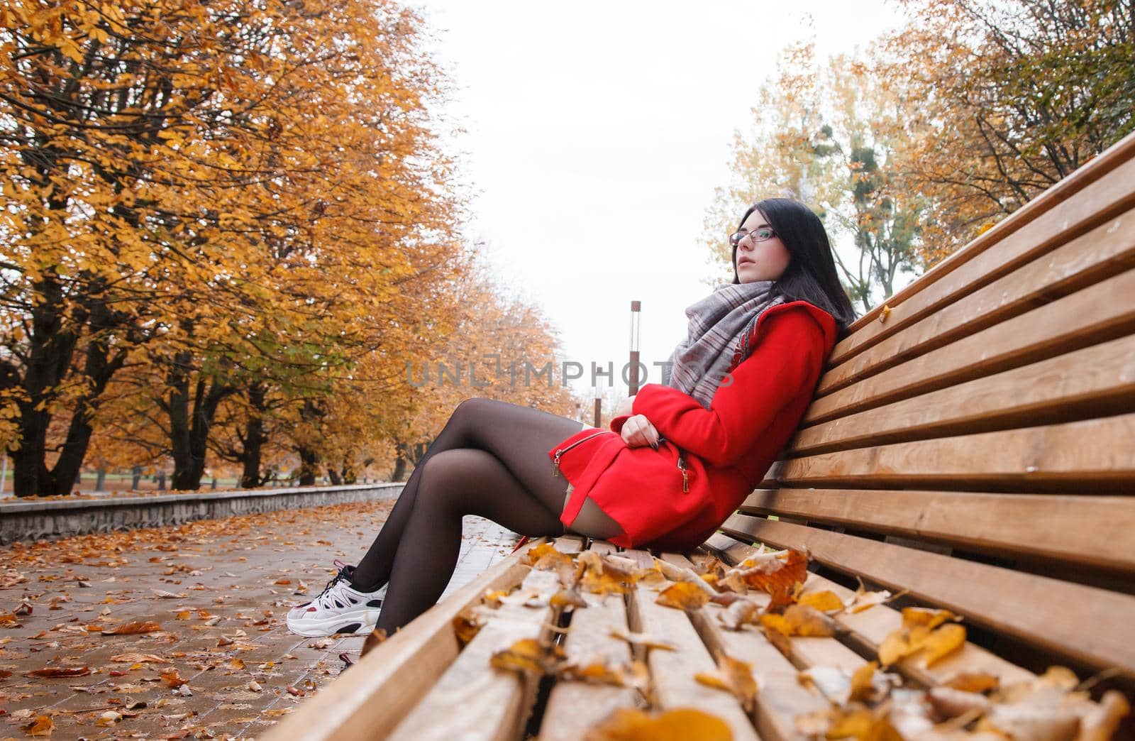 young girl in a red coat sitting on a bench in a city park by raddnatt