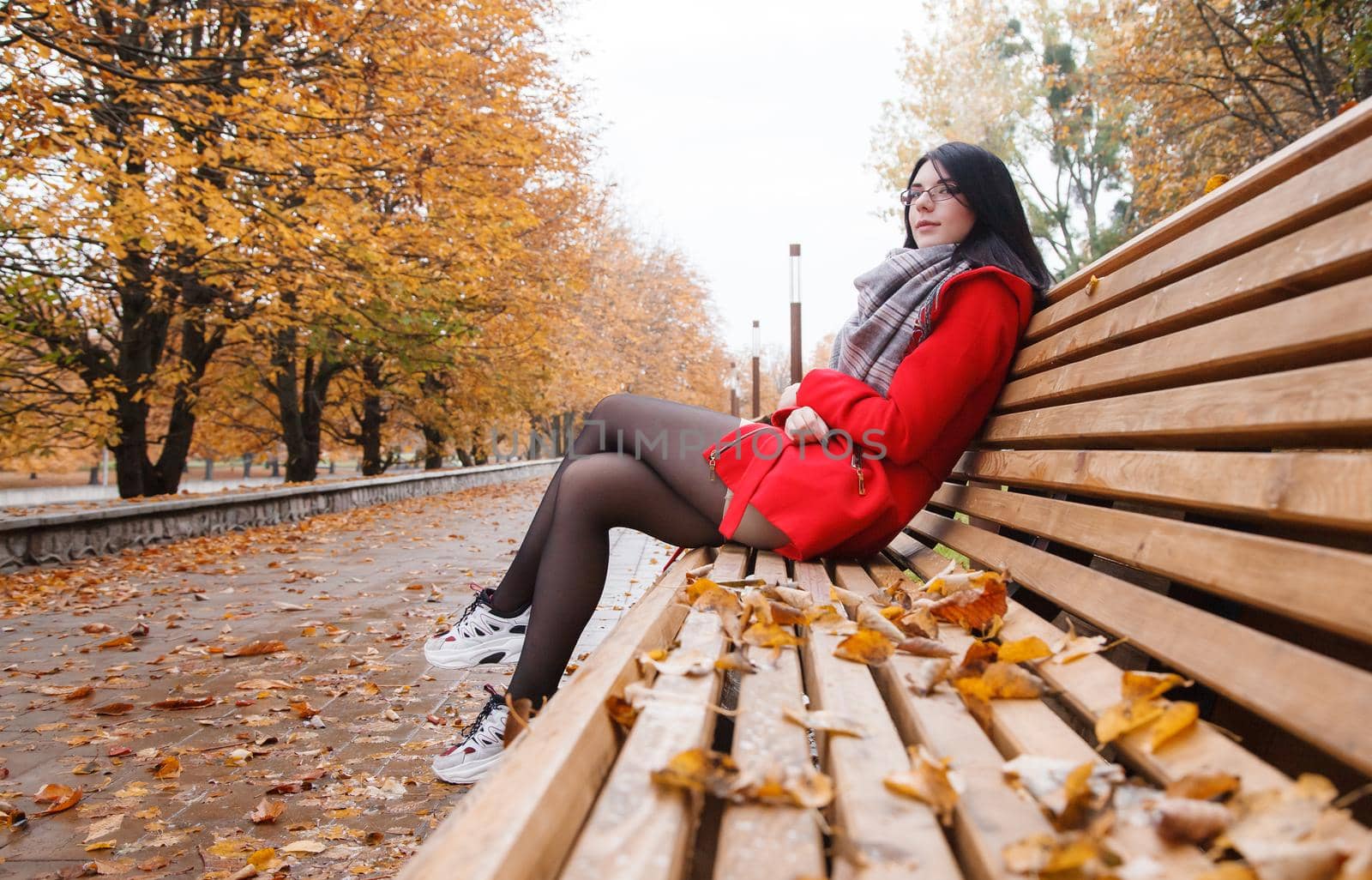 young girl in a red coat sitting on a bench in a city park by raddnatt