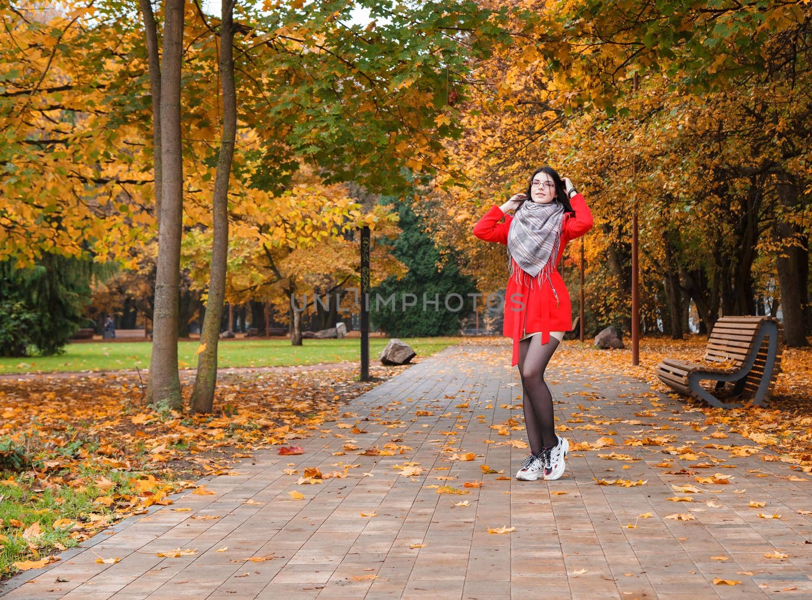 young girl in a red coat standing on the alley of a city park on a autumn day