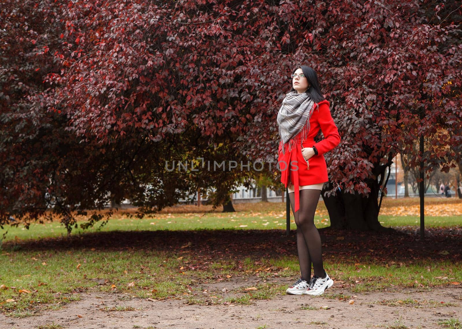 young girl in a red coat standing on the alley of a city park on a autumn day