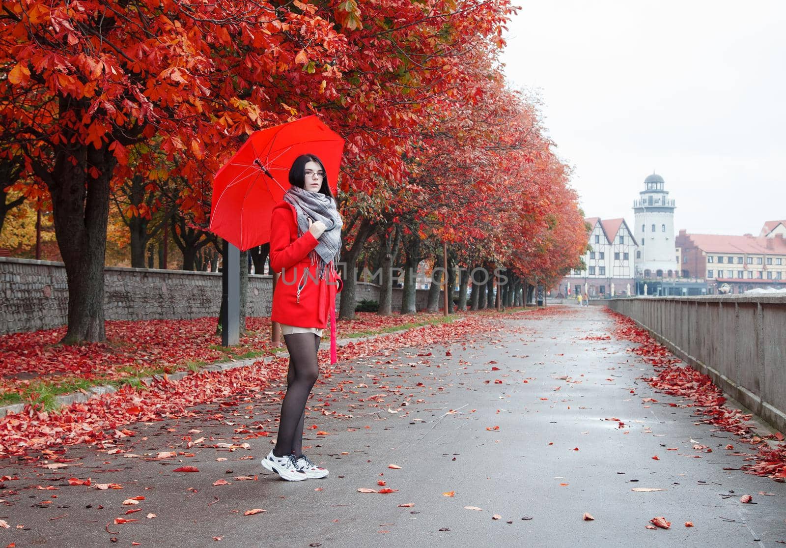 young girl in a red coat with an umbrella standing on the alley of a city park on a autumn day