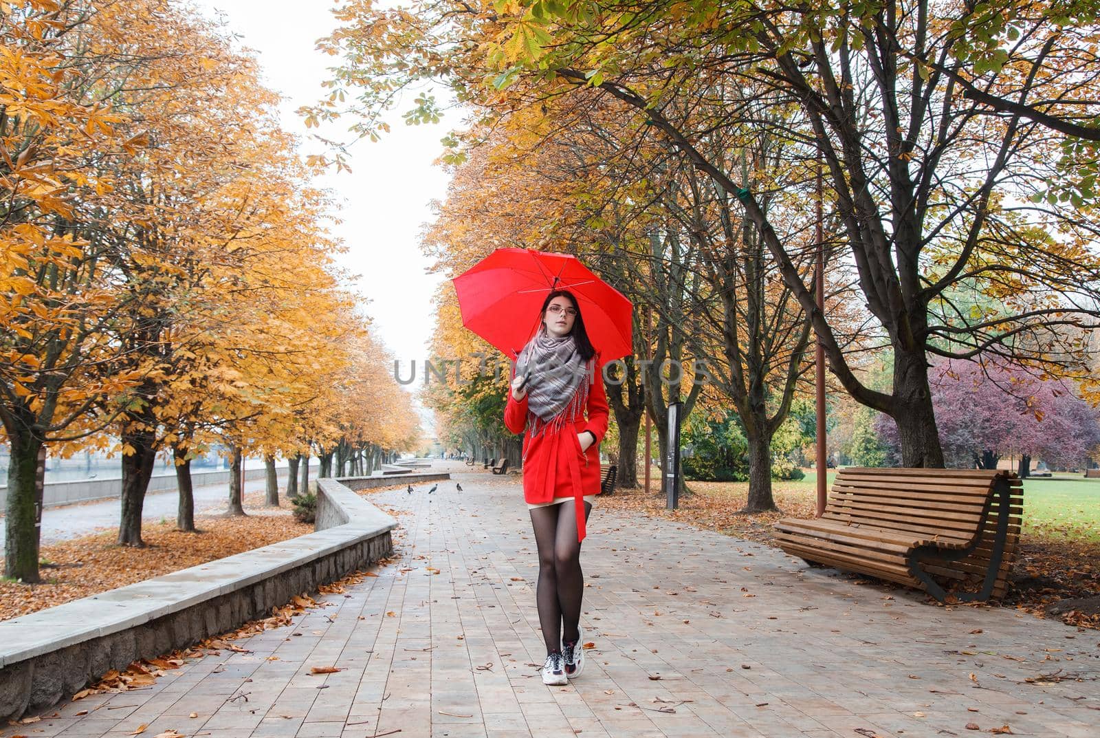 young girl in a red coat with an umbrella walking on the alley by raddnatt