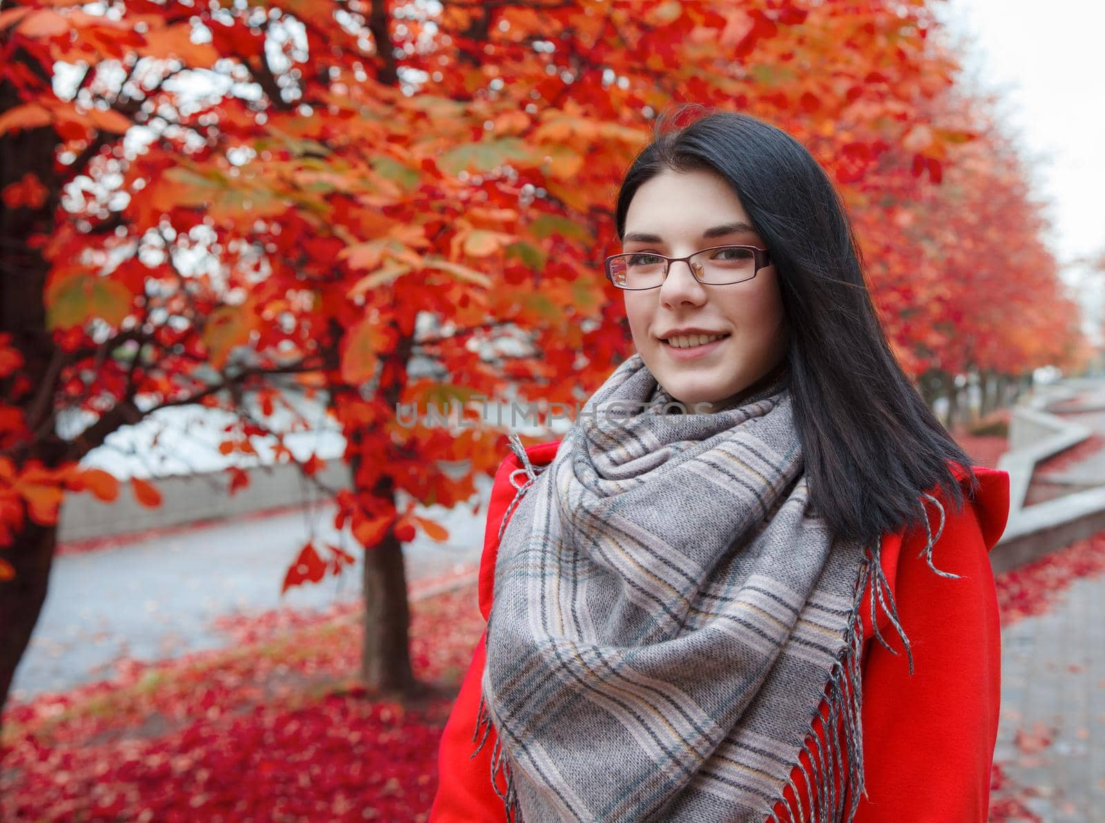 portrait of young smiling girl in a red coat standing on the alley of the park on an autumn day