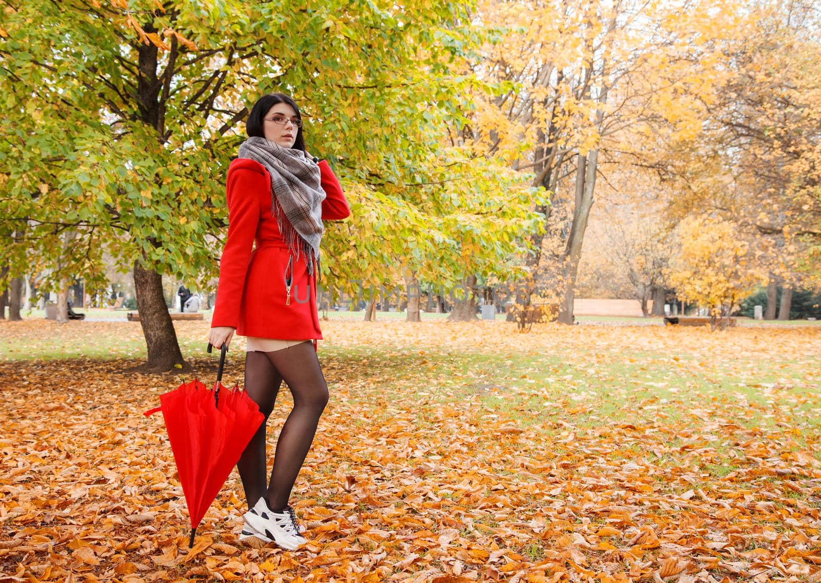 young girl in a red coat with an umbrella standing on the alley of a city park on a sunny autumn day