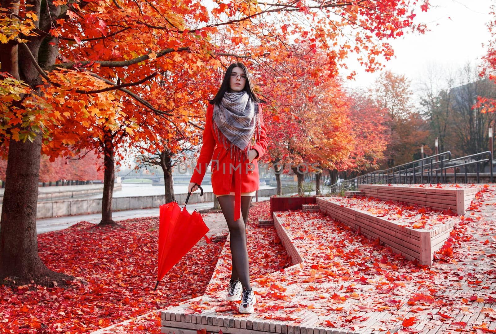 young girl in a red coat with an umbrella standing on the alley of a city park on a sunny autumn day