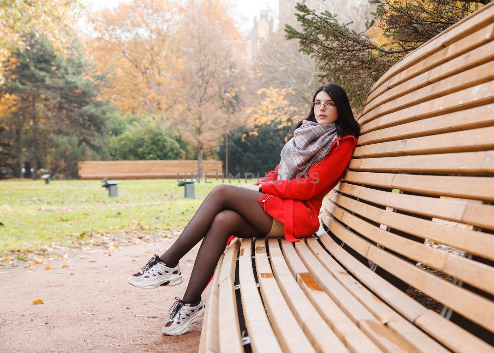 young beautiful girl in a red coat sitting on a bench in a city park after the rain on an autumn day