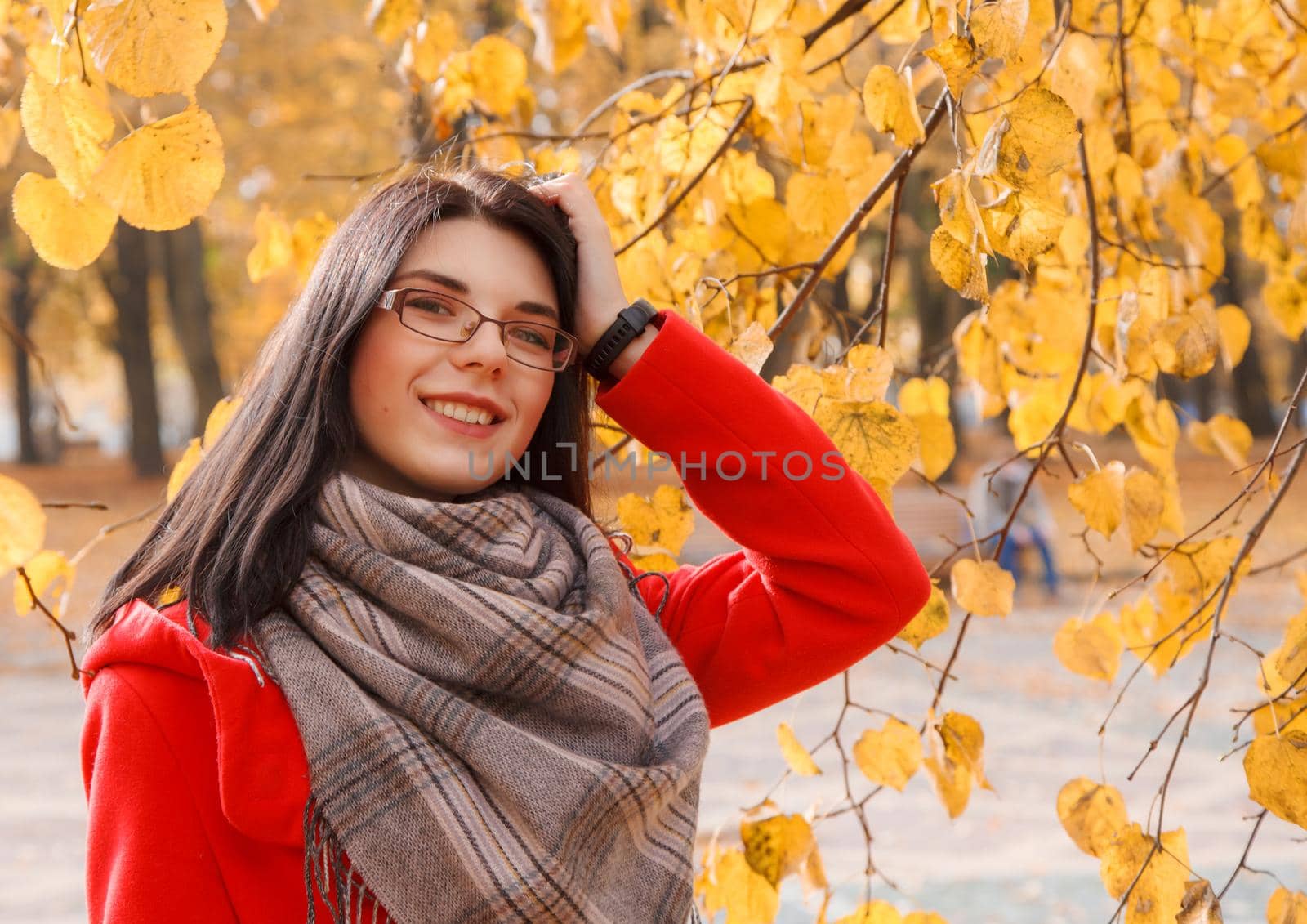 portrait of young smiling girl in a red coat standing on the alley of the park on an autumn day