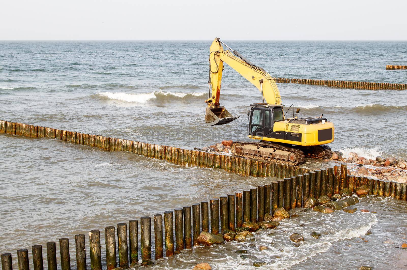 excavator during the construction of a breakwater by the sea on autumn day