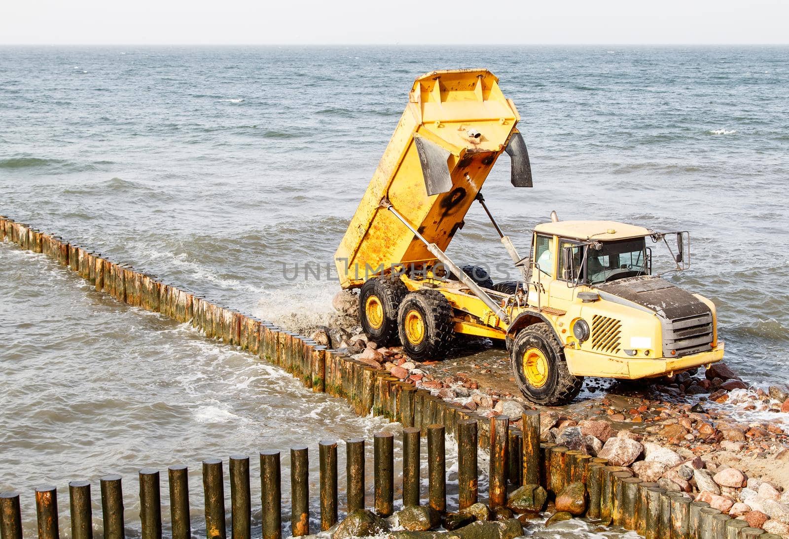 heavy truck during the construction of a breakwater by the sea on autumn day