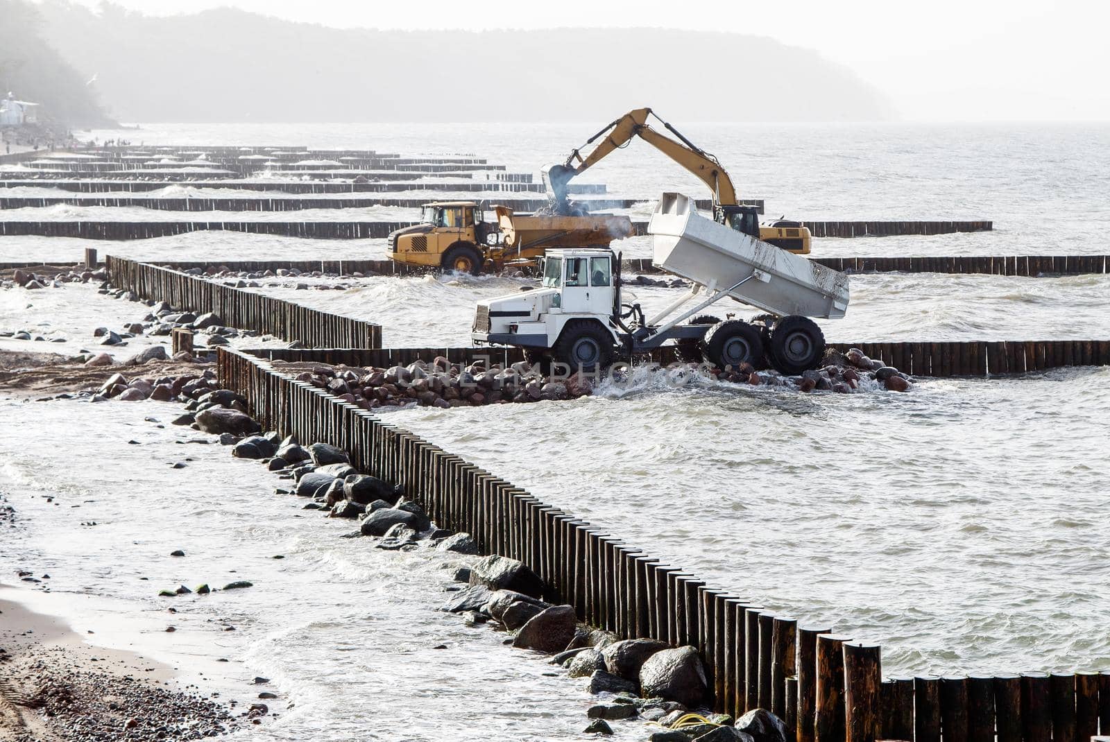 excavator loading soil into a large truck during the construction of a breakwater on the seashore on autumn day