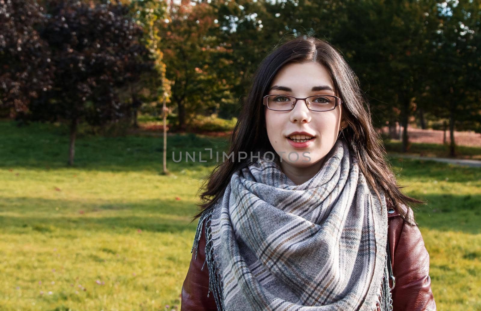 portrait of a young beautiful smiling girl in brown jacket in city park on sunny autumn day
