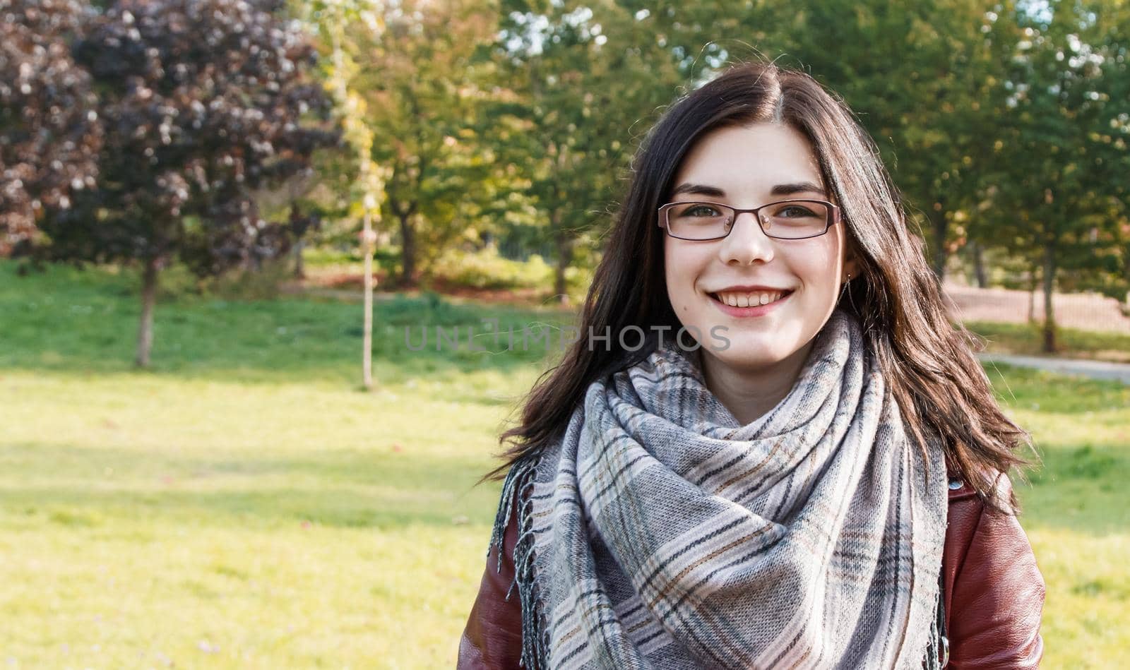portrait of a young beautiful smiling girl in brown jacket in city park on sunny autumn day