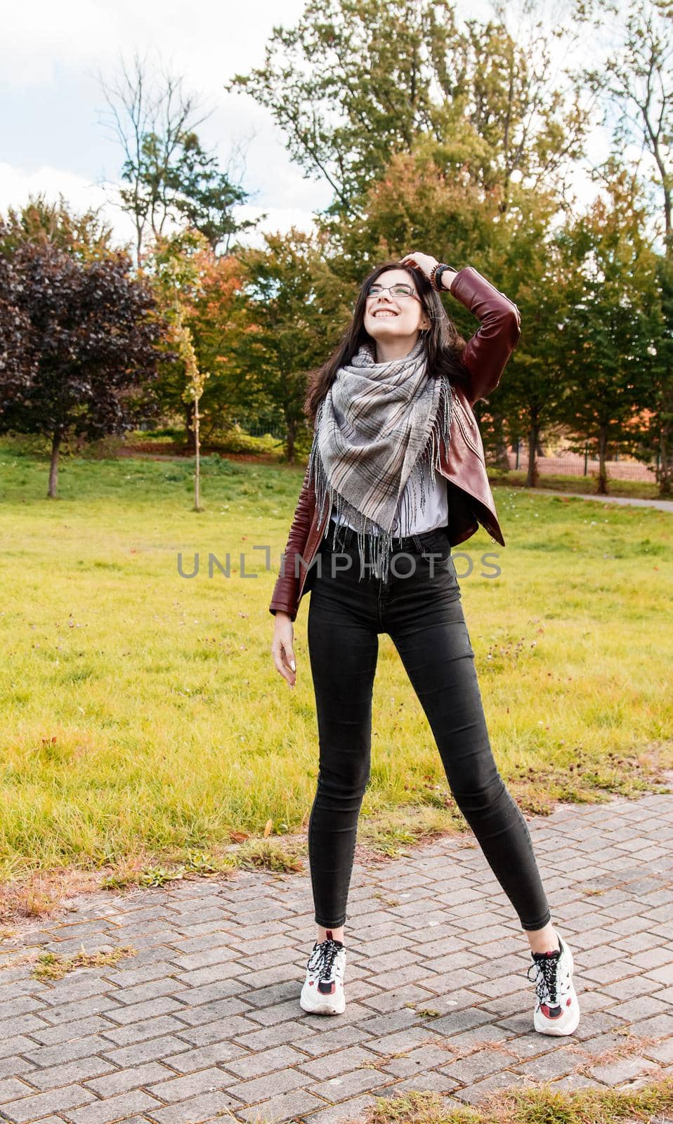 young girl in brown jacket and black jeans standing on the alley in city park on sunny autumn day