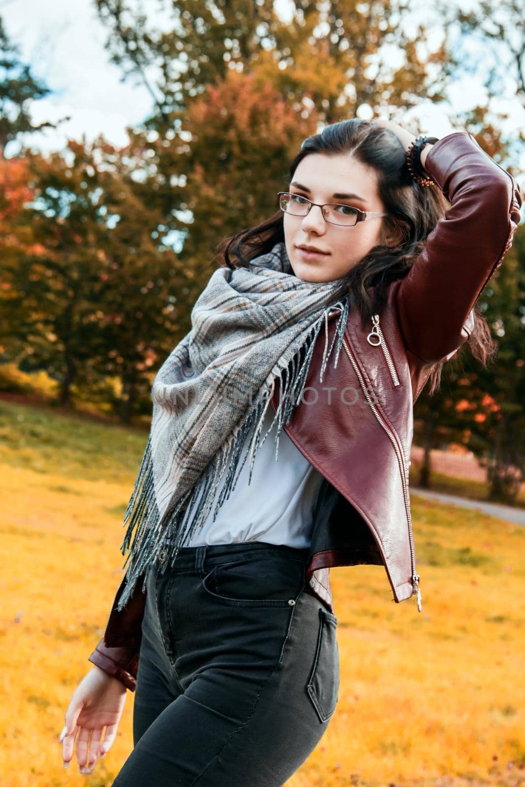 young girl in brown jacket and black jeans standing on the alley in city park on sunny autumn day