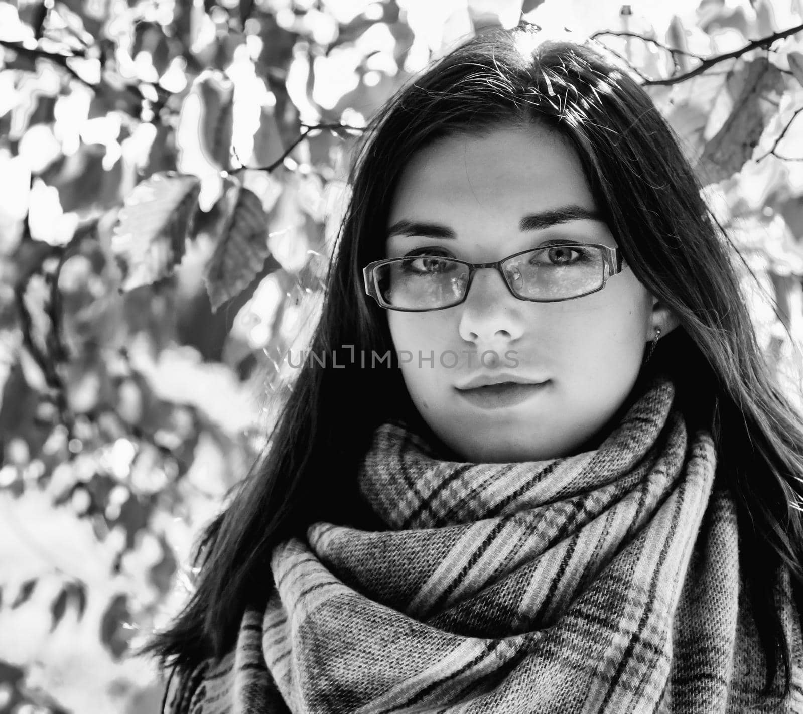 portrait of a young beautiful girl in brown jacket in city park on sunny autumn day. black and white