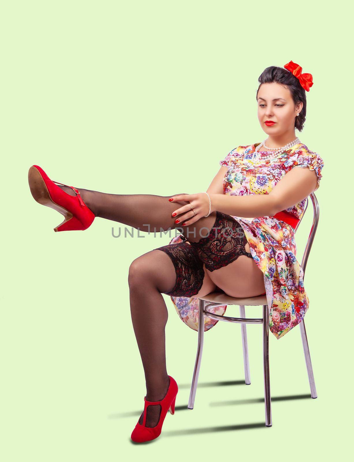 woman straightens her stocking while sitting on a chair in studio. pinup style