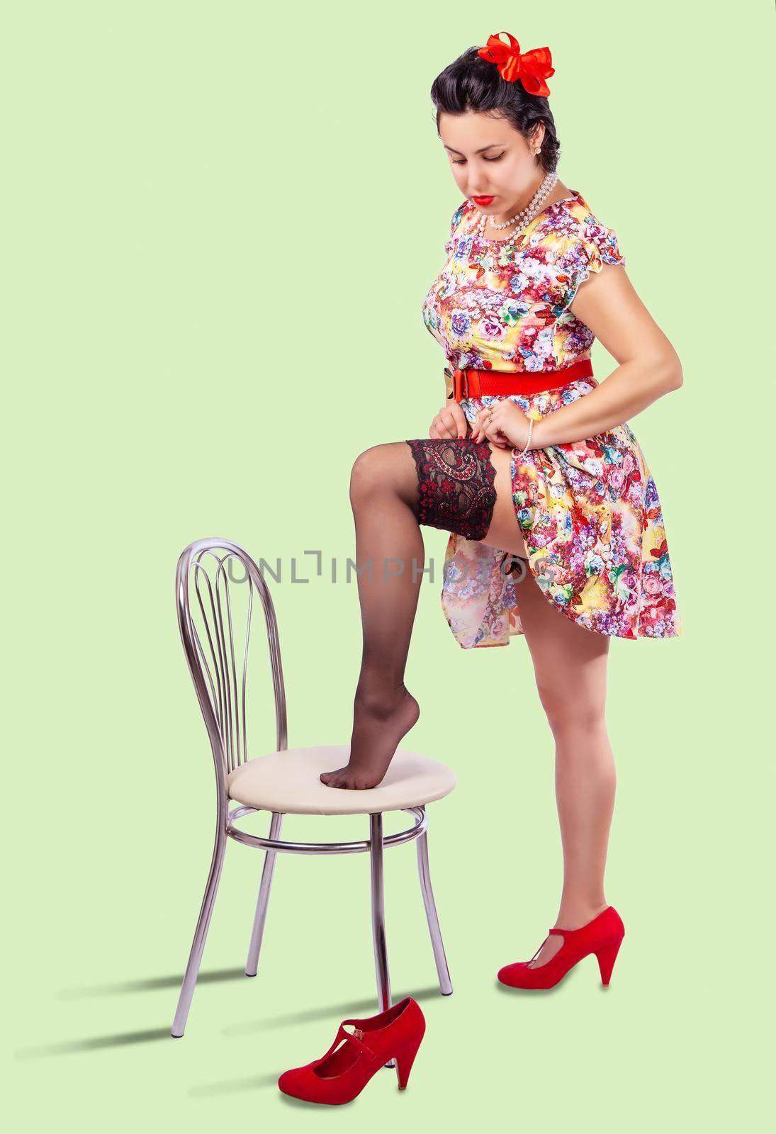 young woman straightens her stocking by placing her leg on the chair. pinup style