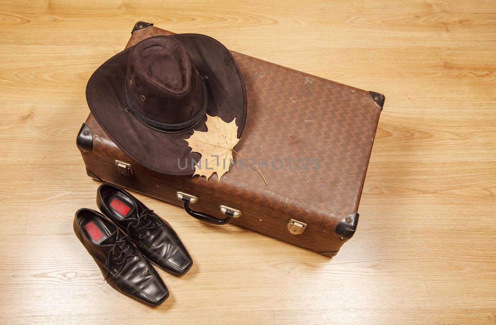 set of men's felt hat with a yellow maple leaf, black shoes and a suitcase on a wooden floor