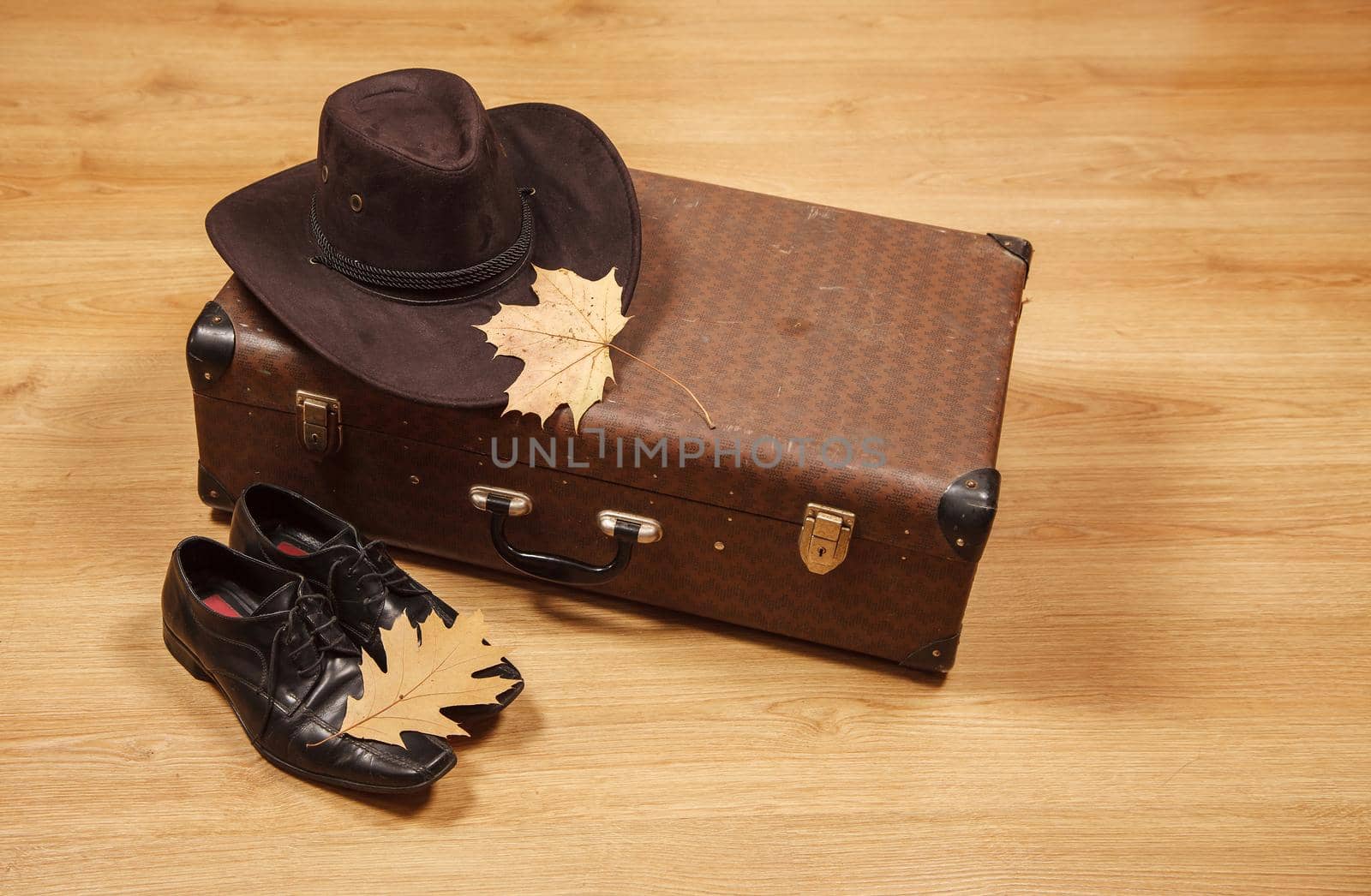set of men's felt hat with a yellow maple leaf, black shoes and a suitcase on a wooden floor