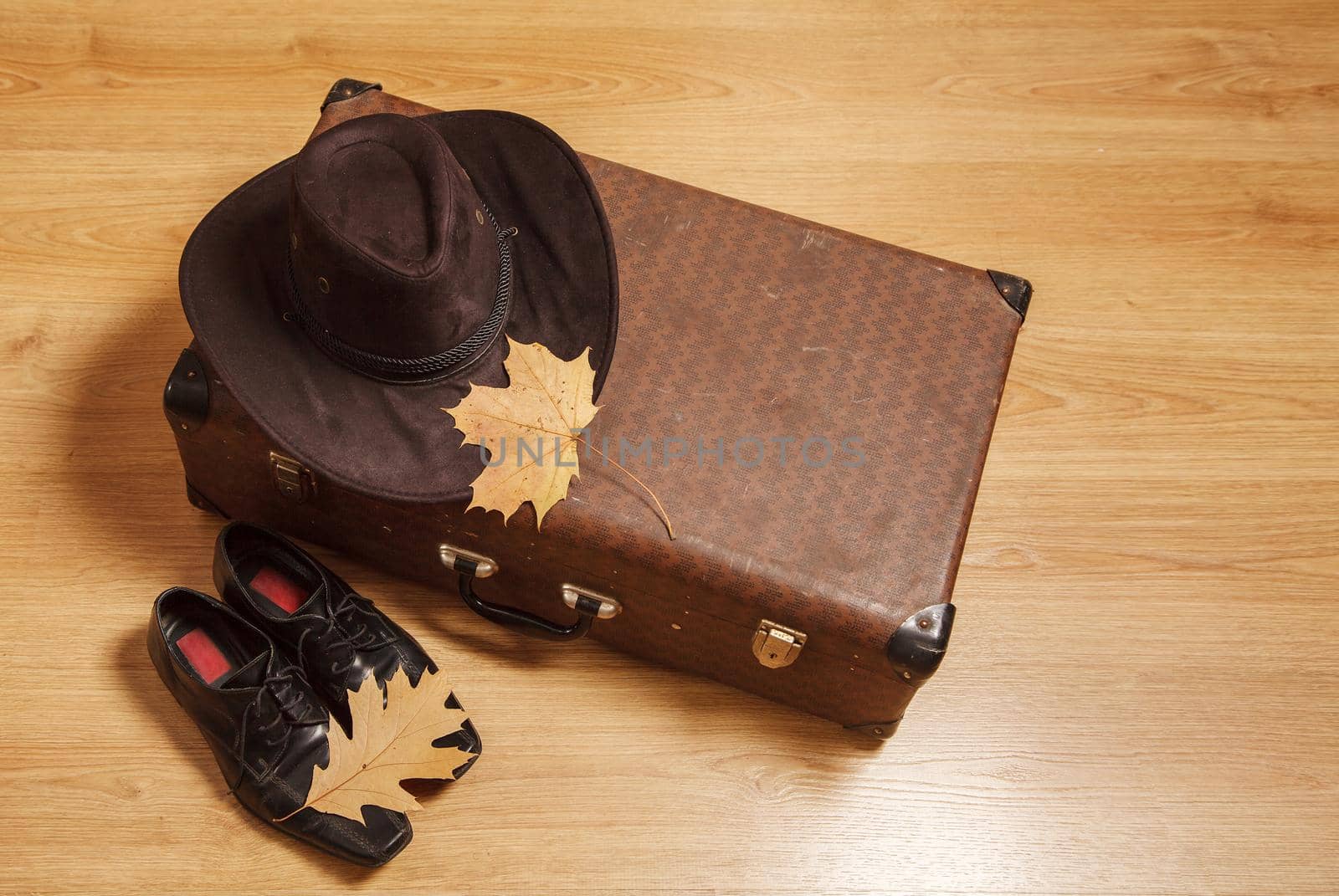 set of men's felt hat with a yellow maple leaves, black shoes and a suitcase on a wooden floor