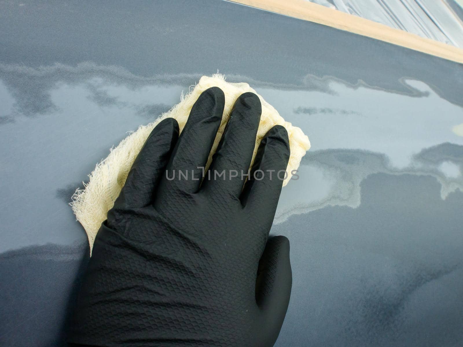 the hand of the auto painter in a black glove holds a special napkin for dusting the surface of the car. by igor707