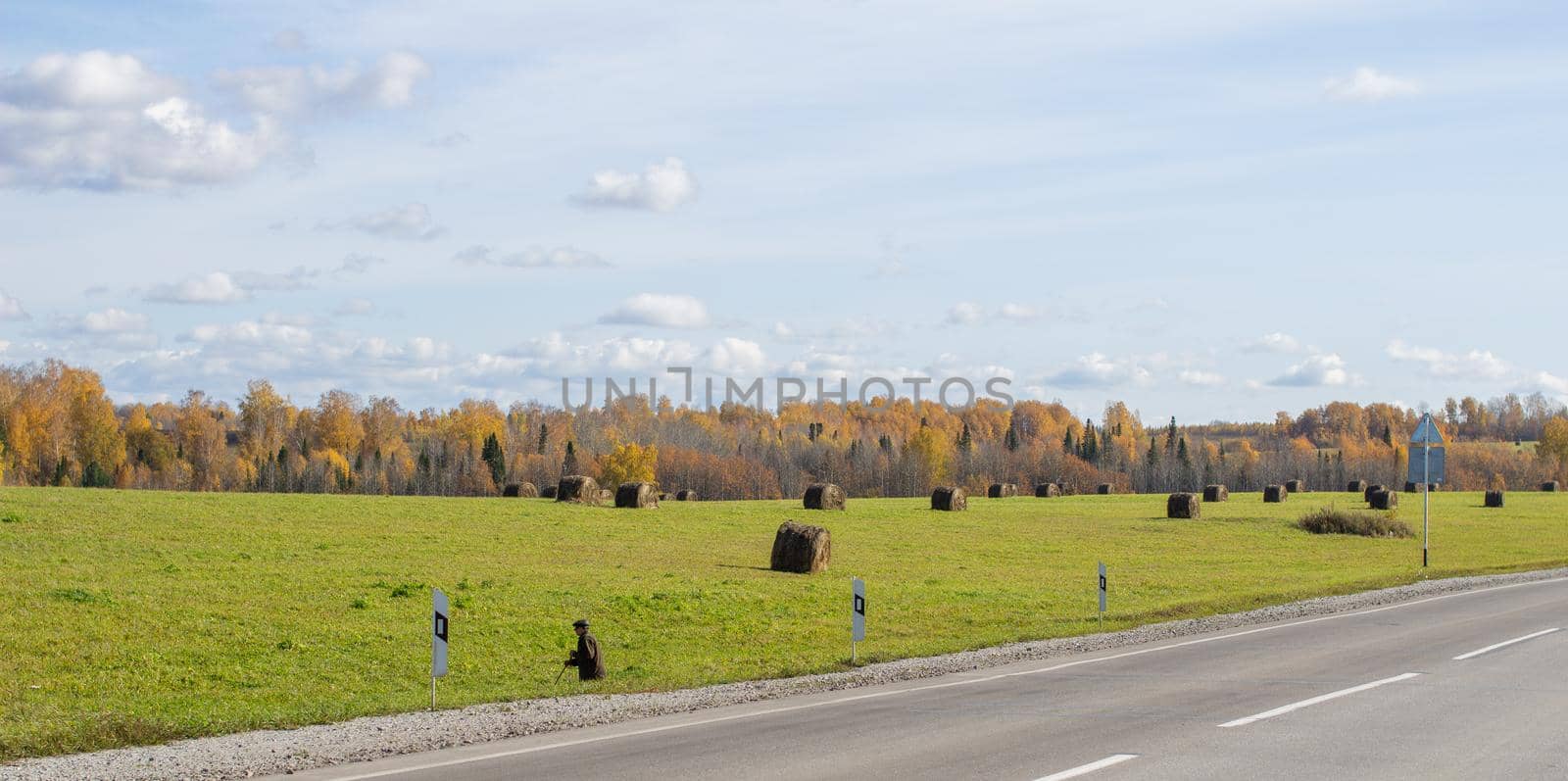Road between fields with hay bales in autumn. Agricultural field with sky and clouds. The nature of agriculture. Straw in the meadow. Rural natural landscape. The harvest of grain and the harvest.