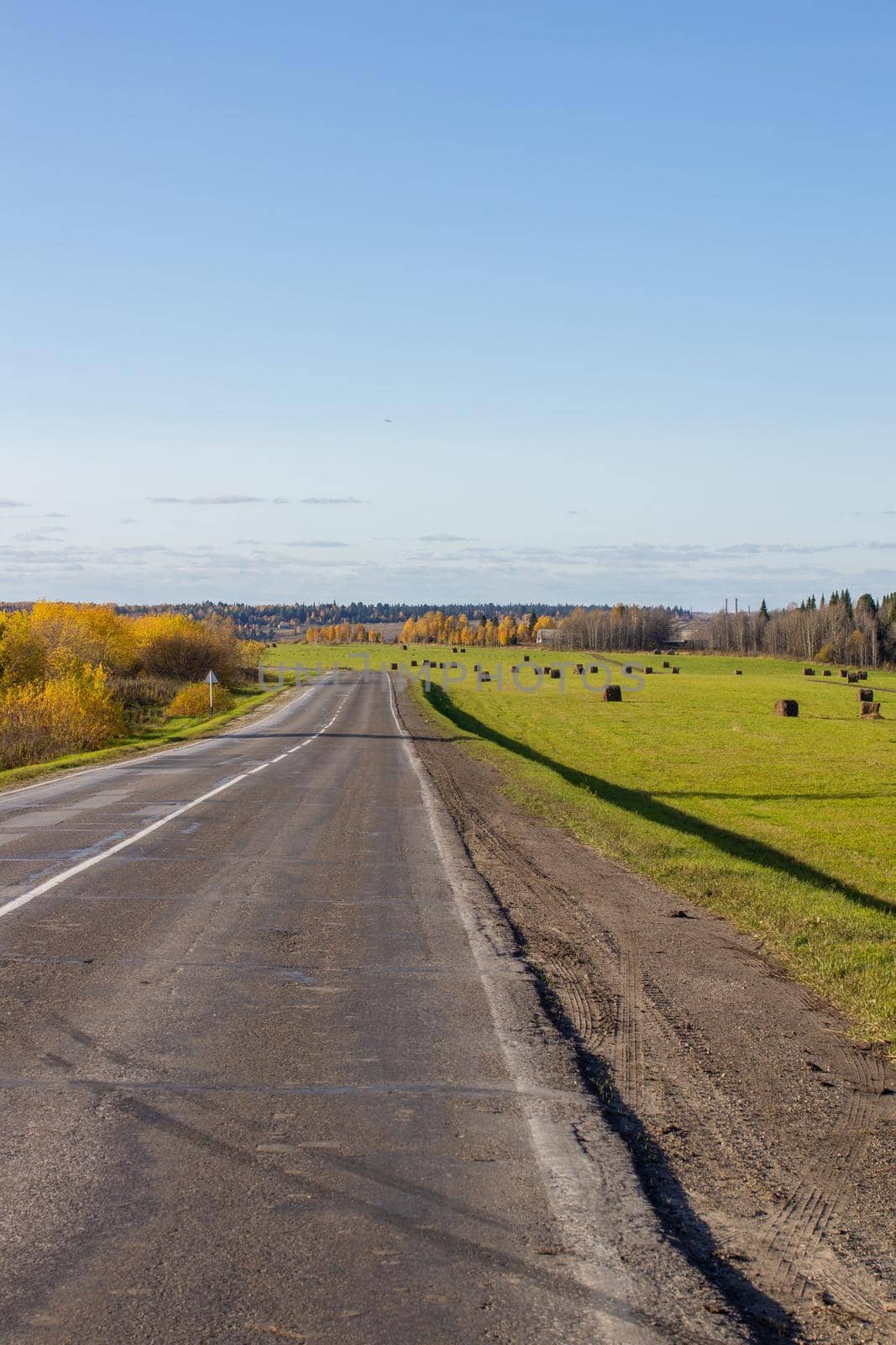 Road between fields with hay bales in autumn. Agricultural field with sky and clouds. The nature of agriculture. Straw in the meadow. Rural natural landscape. The harvest of grain and the harvest.