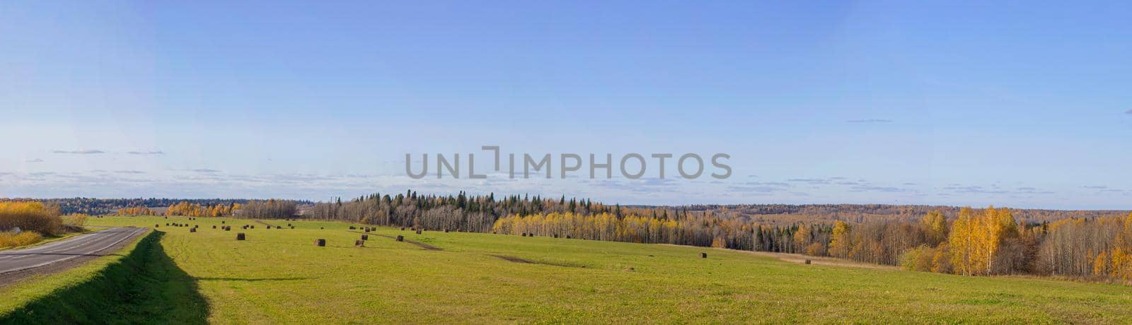 Road between fields with hay bales in autumn. Agricultural field with sky and clouds. The nature of agriculture. Straw in the meadow. Rural natural landscape. The harvest of grain and the harvest.