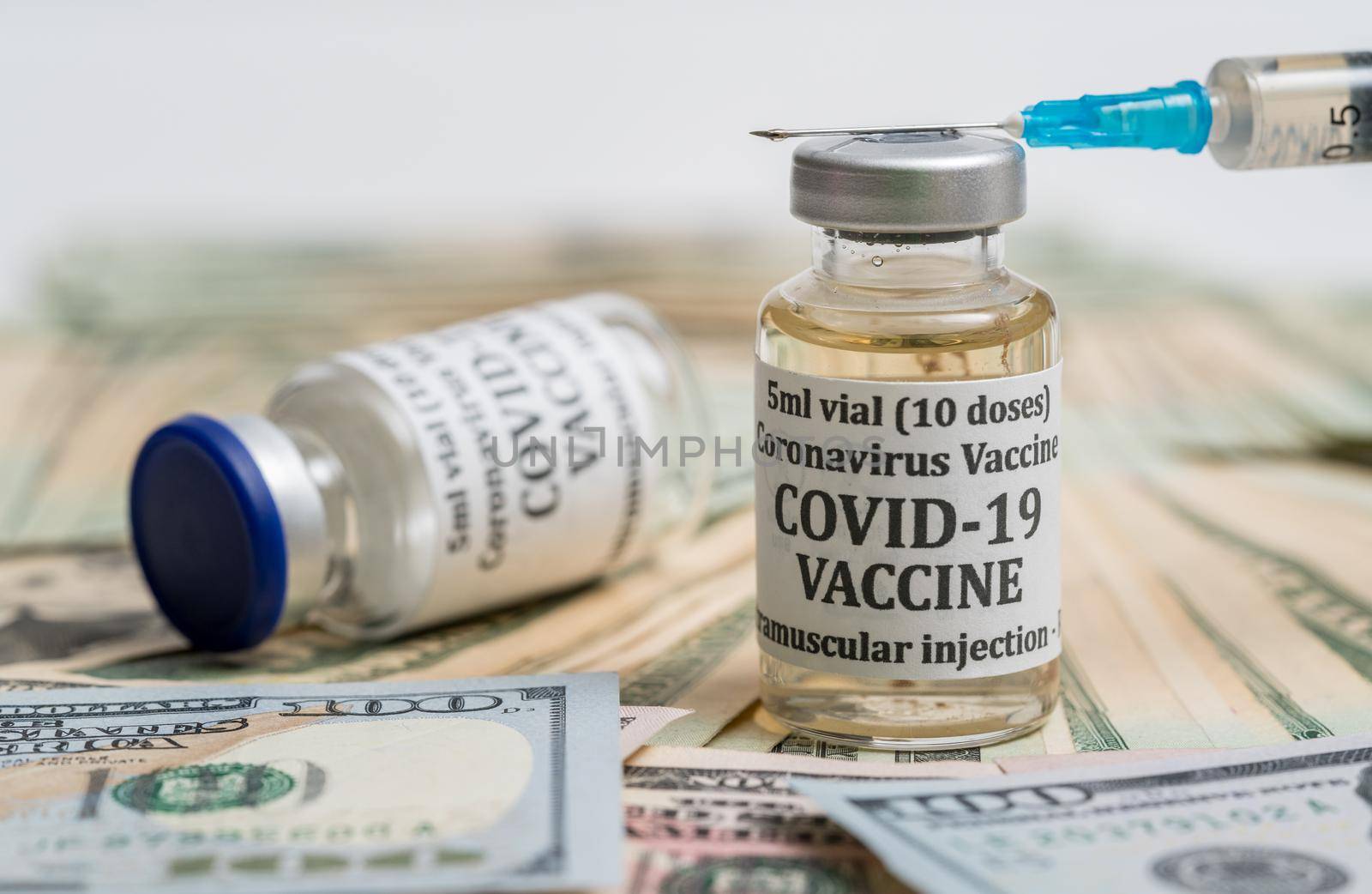 Covid-19 coronavirus vaccine with hypodermic syringe needle sitting on pile of cash to suggest payment to get the vaccination