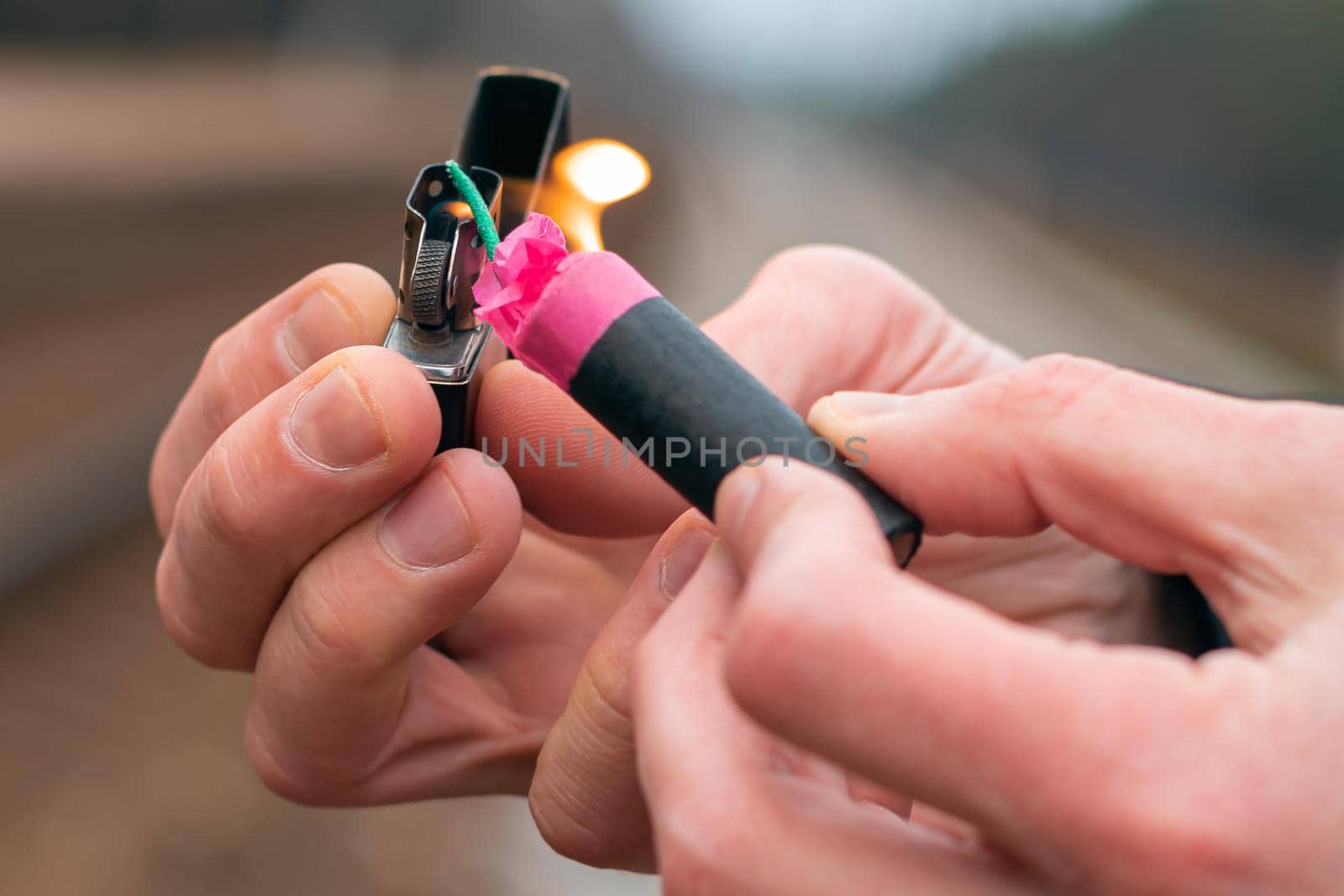 Setting Fire to the Firecracker. Man in Black Clothes Lighting Up the Petard. Firing Up the Pyrotechnics with a Black Gasoline Lighter Outdoors