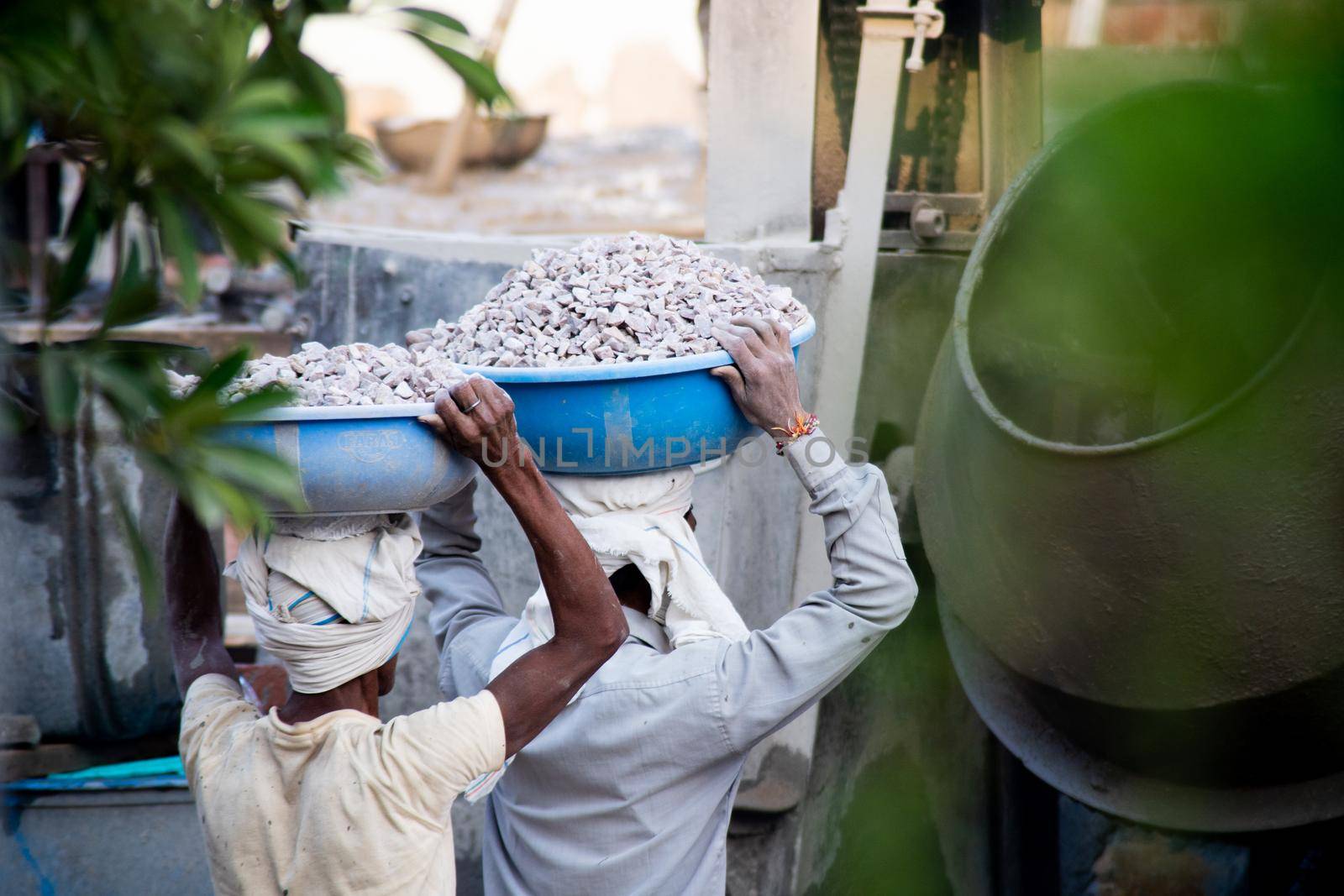 zoomed in shot of indian underprivleged construction workers carrying sand, cement, stones and water on their head to load into a mixer to make concrete for the making of infrastructure real estate, homes and offices in India by Shalinimathur