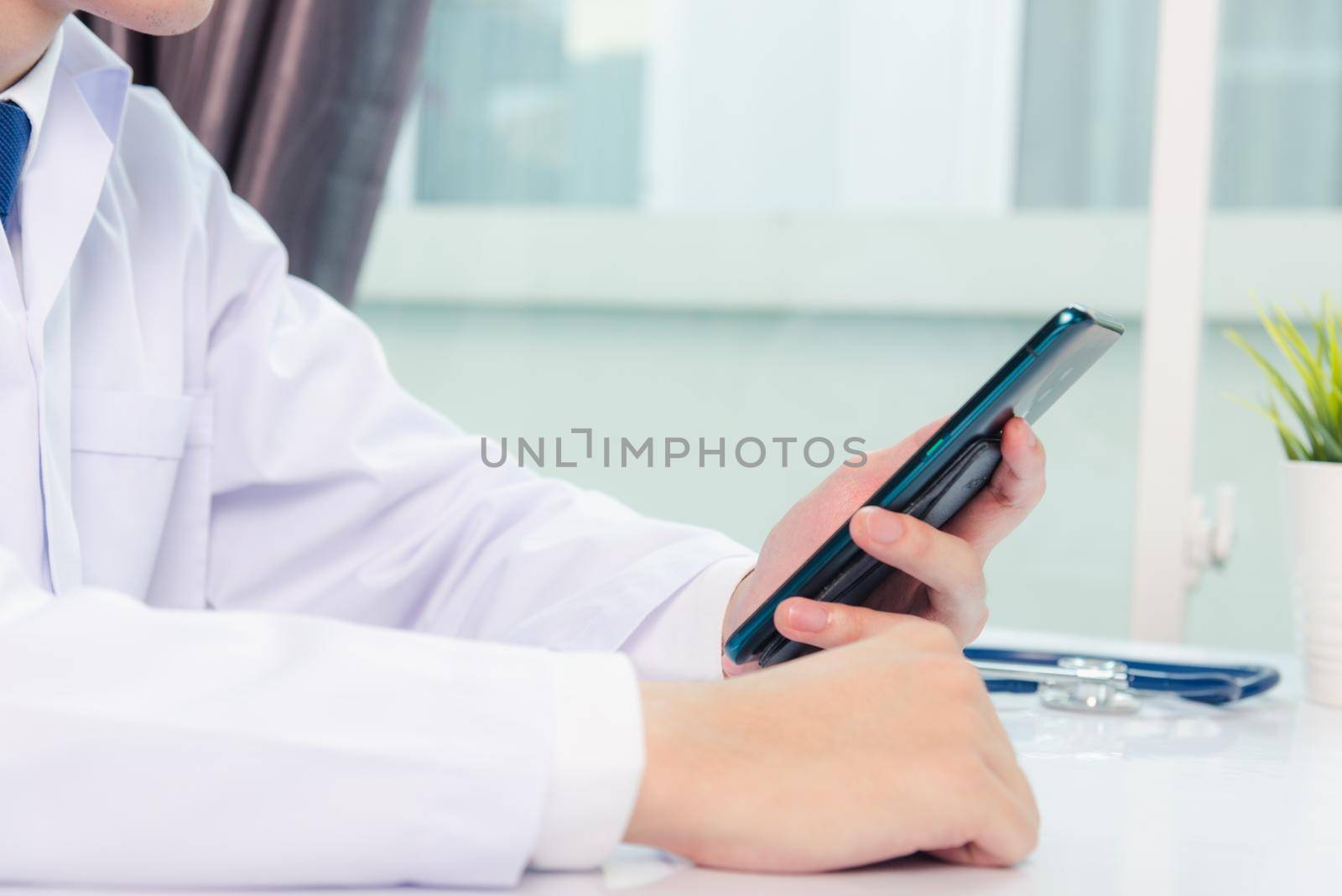 Asian doctor young handsome man smiling using working or holding with digital smart mobile phone at hospital desk office, Technology healthcare medical concept