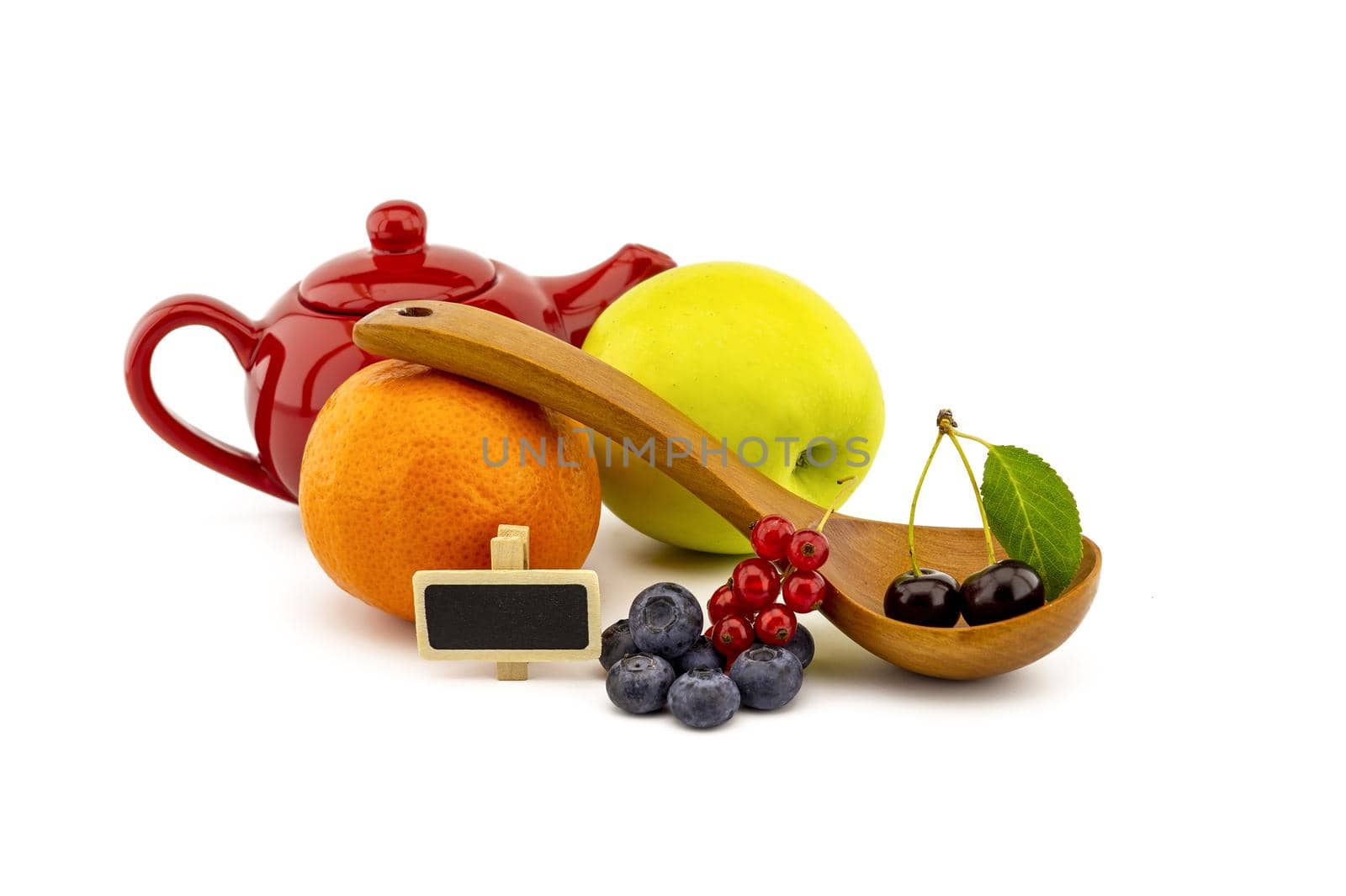 Fresh seasonal fruit still life with assorted berries including blueberries, cherries and red currants on wooden spoons with apple and orange and colorful red teapot