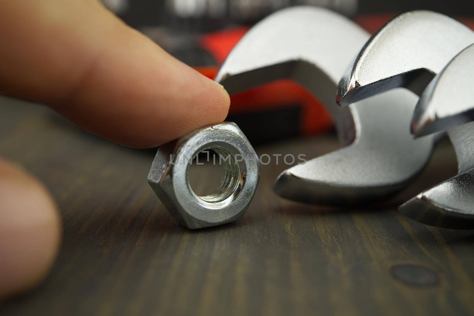Finger holds the single metal nut next to set of spanners or wrenches