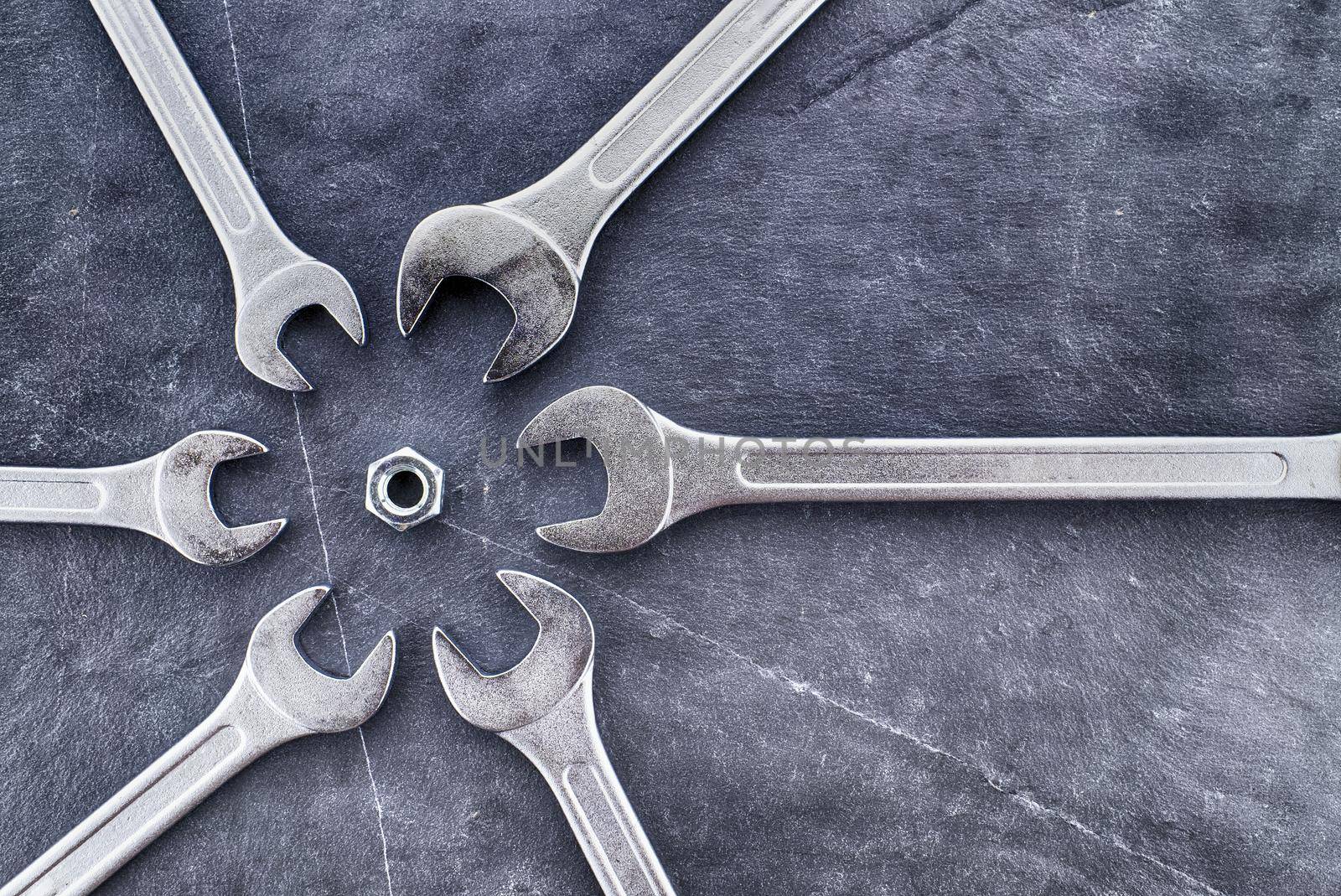 Circle of spanners or wrenches surrounding a nut on a grunge stone surface, top view