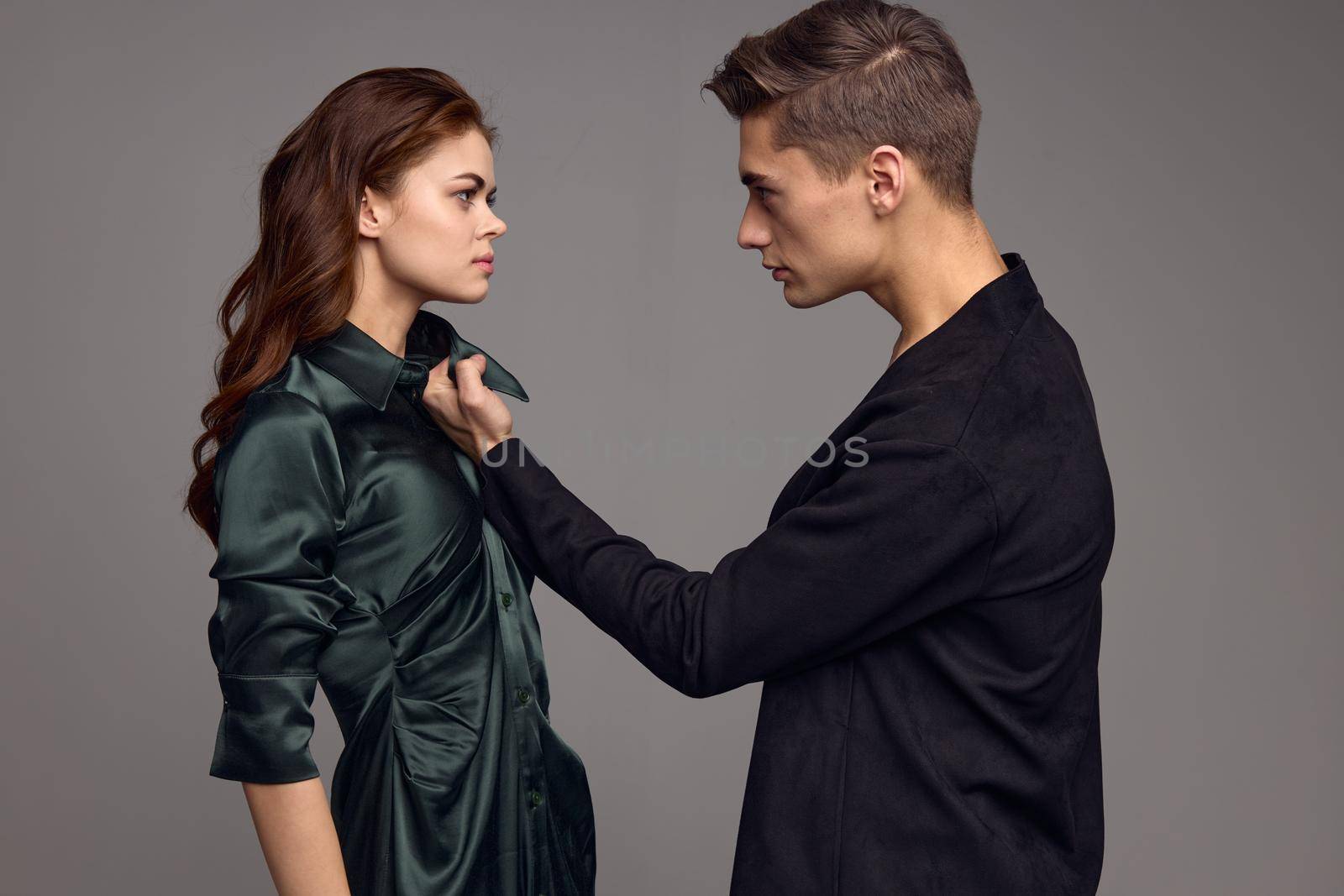 Aggressive man in a suit holds a woman by the collar of a dress on a gray background. High quality photo