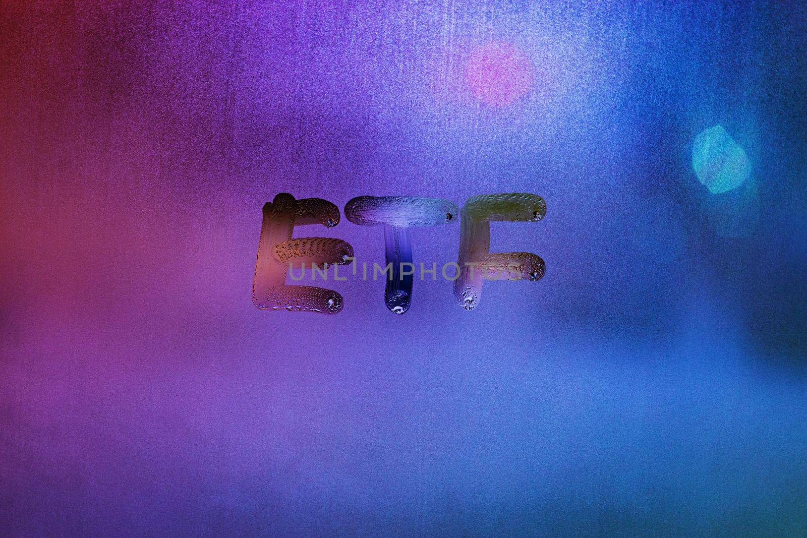 abbreviation word etf - exchange traded funds - handwritten on foggy glass window at night with neon blue back street lights