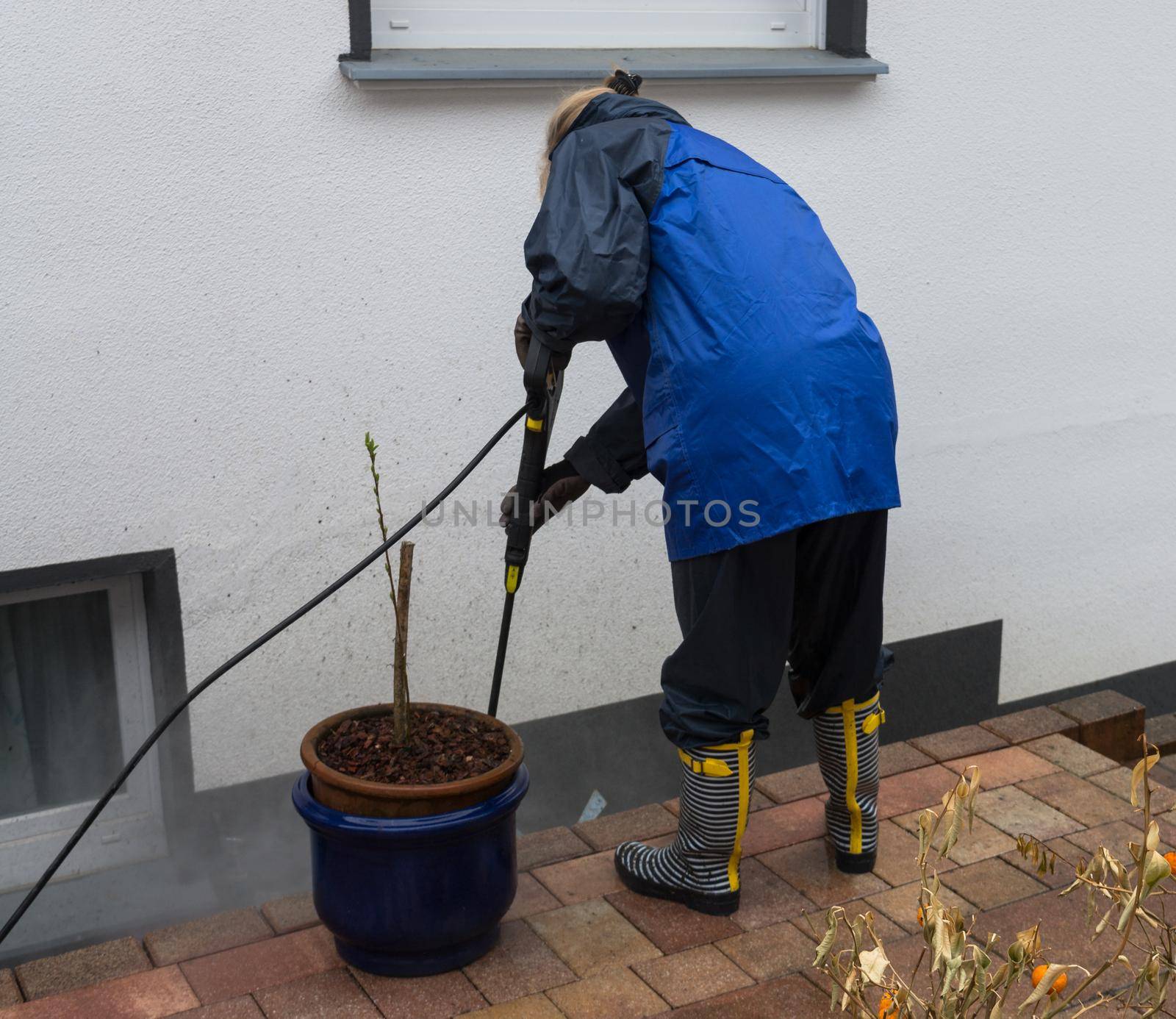 Woman cleans stone slabs with a pressure washer