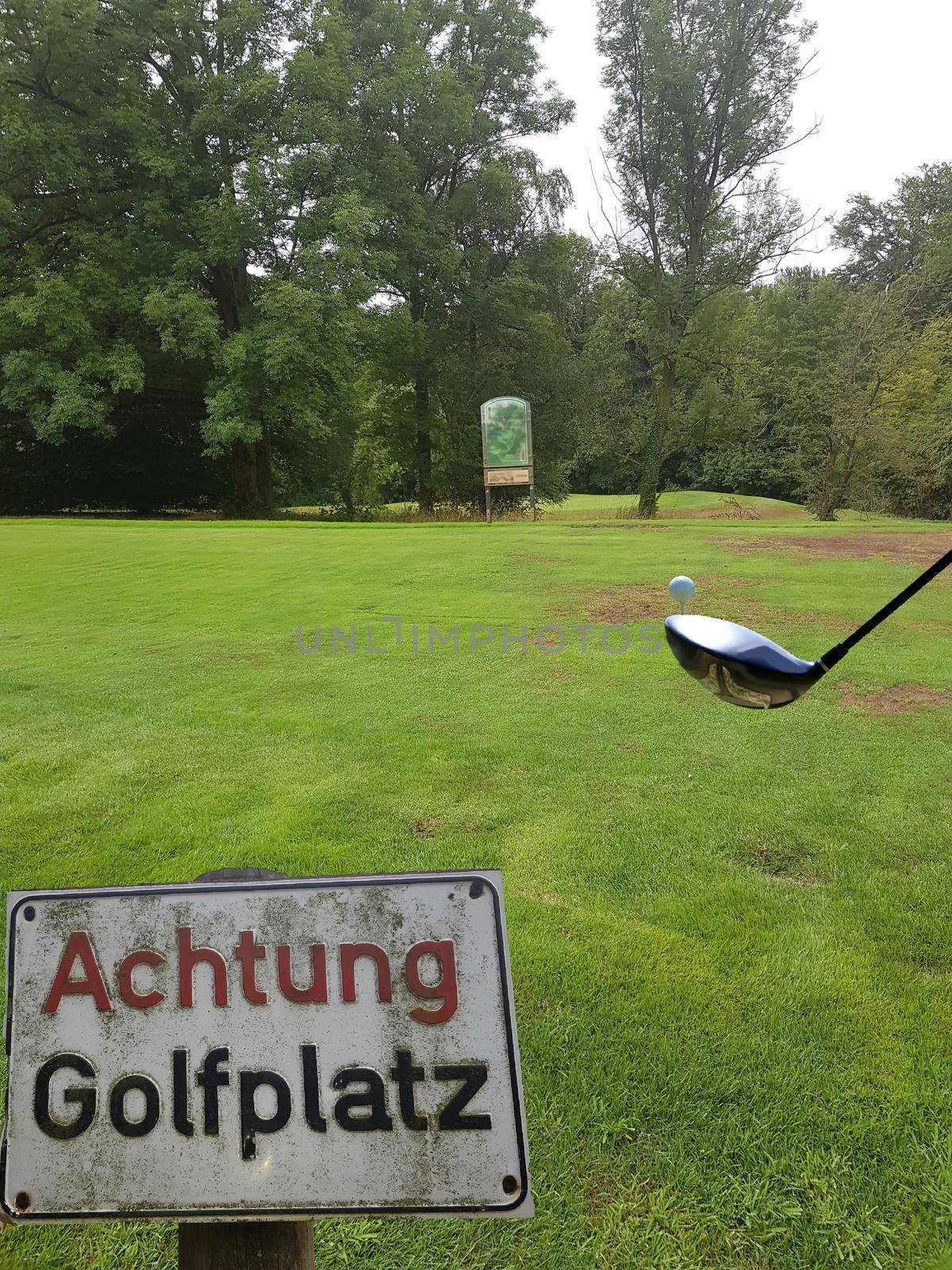 Rectangular sign with inscription in German - Caution golf course
in the background the green of a golf course with golf ball and racket. Concept Pitch and Putt