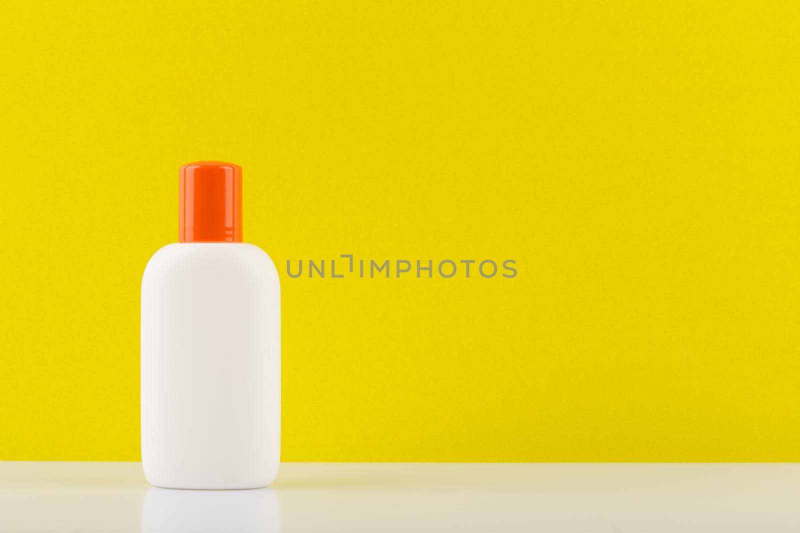 Minimalistic still life with unbranded sunscreen lotion for safe tanning on white table against yellow background with copy space. High quality photo