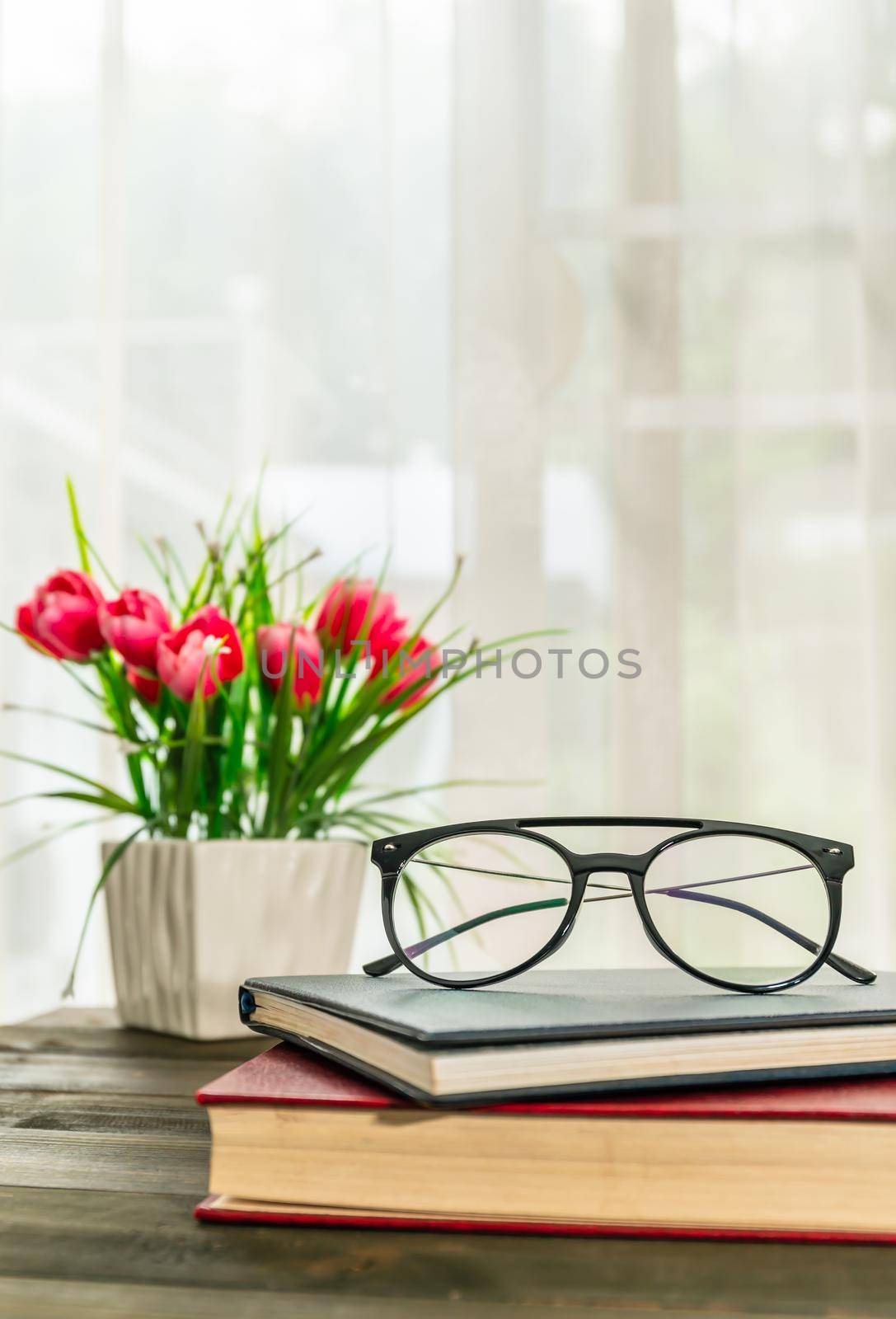 Reading glasses put on hardcover book beside the window by stoonn