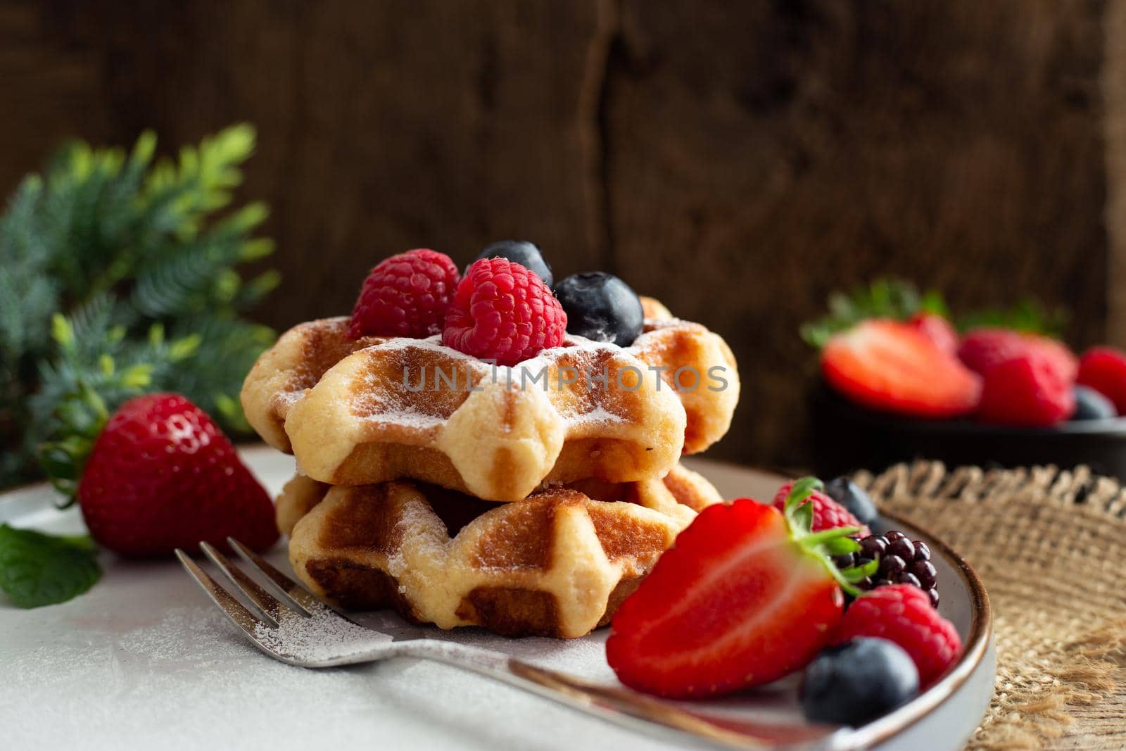 Belgian waffles with strawberries, summer berries on plate with canvas on dark old wooden dramatic background. Horizontal view. Menu, banner, poster, mock up. Rustic vintage style of kitchen.