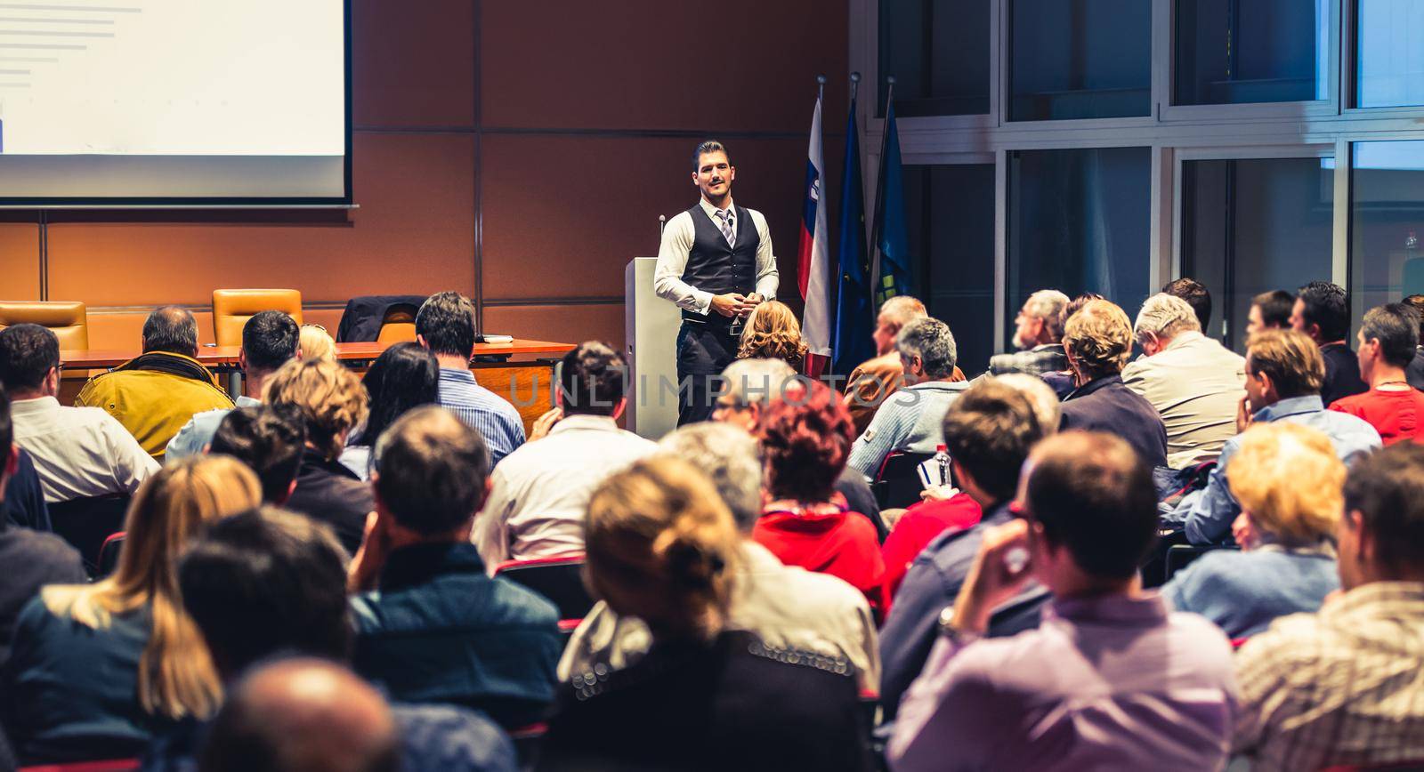 Speaker giving a talk in conference hall at business meeting event. Rear view of unrecognizable people in audience at the conference hall. Business and entrepreneurship concept.