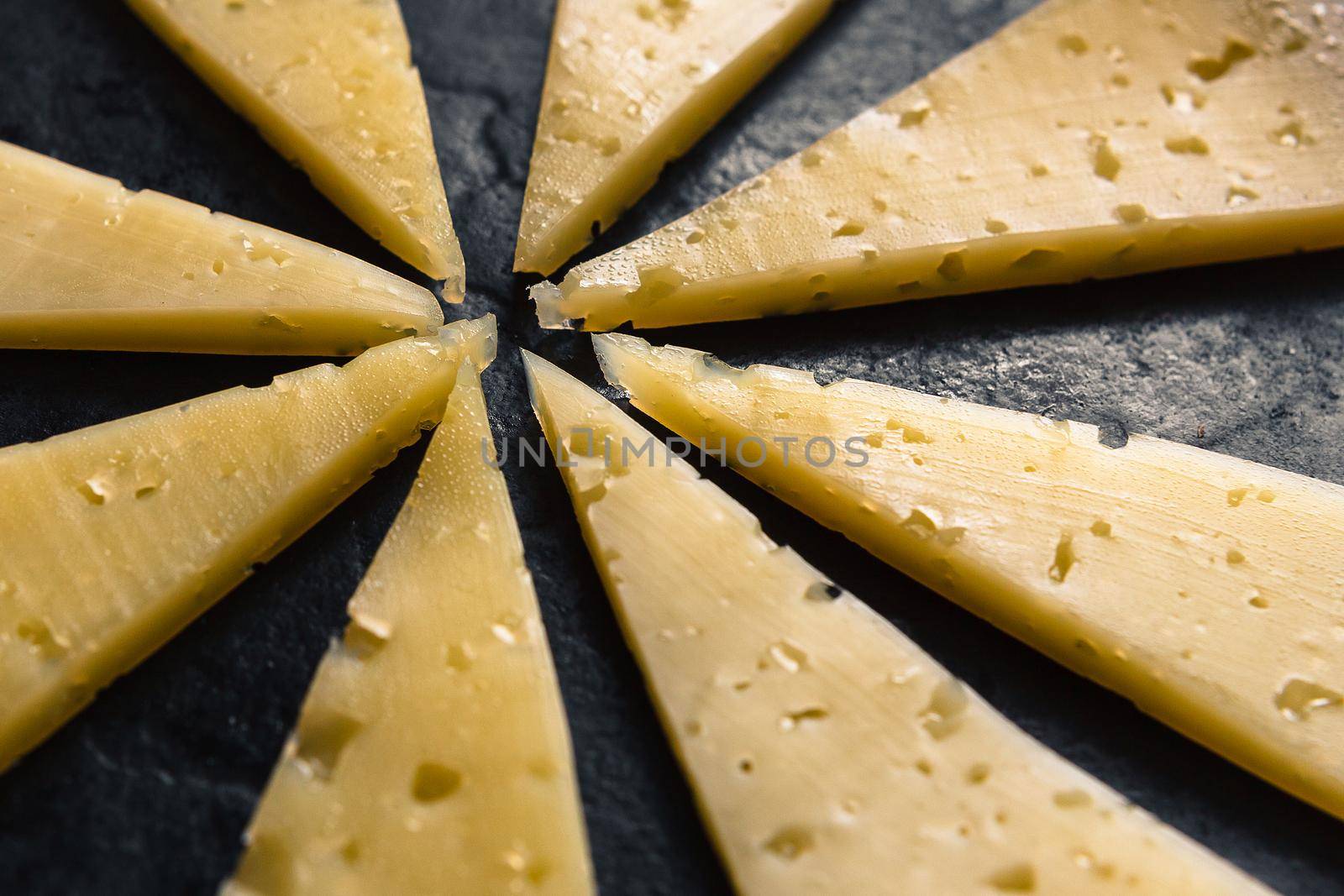Pieces of cheese are laid out in the form of sunlight on a black cast-iron surface.
